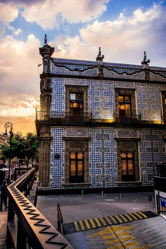 Ornate building with blue and white tile façade, featuring large windows and decorative stonework, under a cloudy sky at sunset.