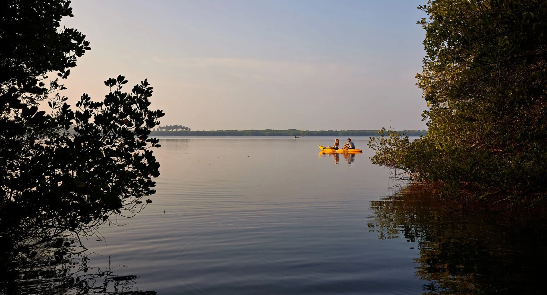 Two people kayaking in a yellow kayak on a calm lake surrounded by trees.