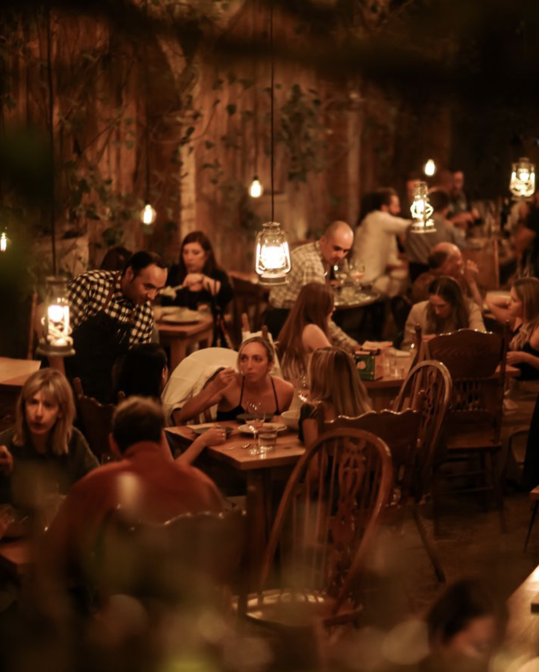 Cozy restaurant with people dining, dim lighting, and rustic decor.