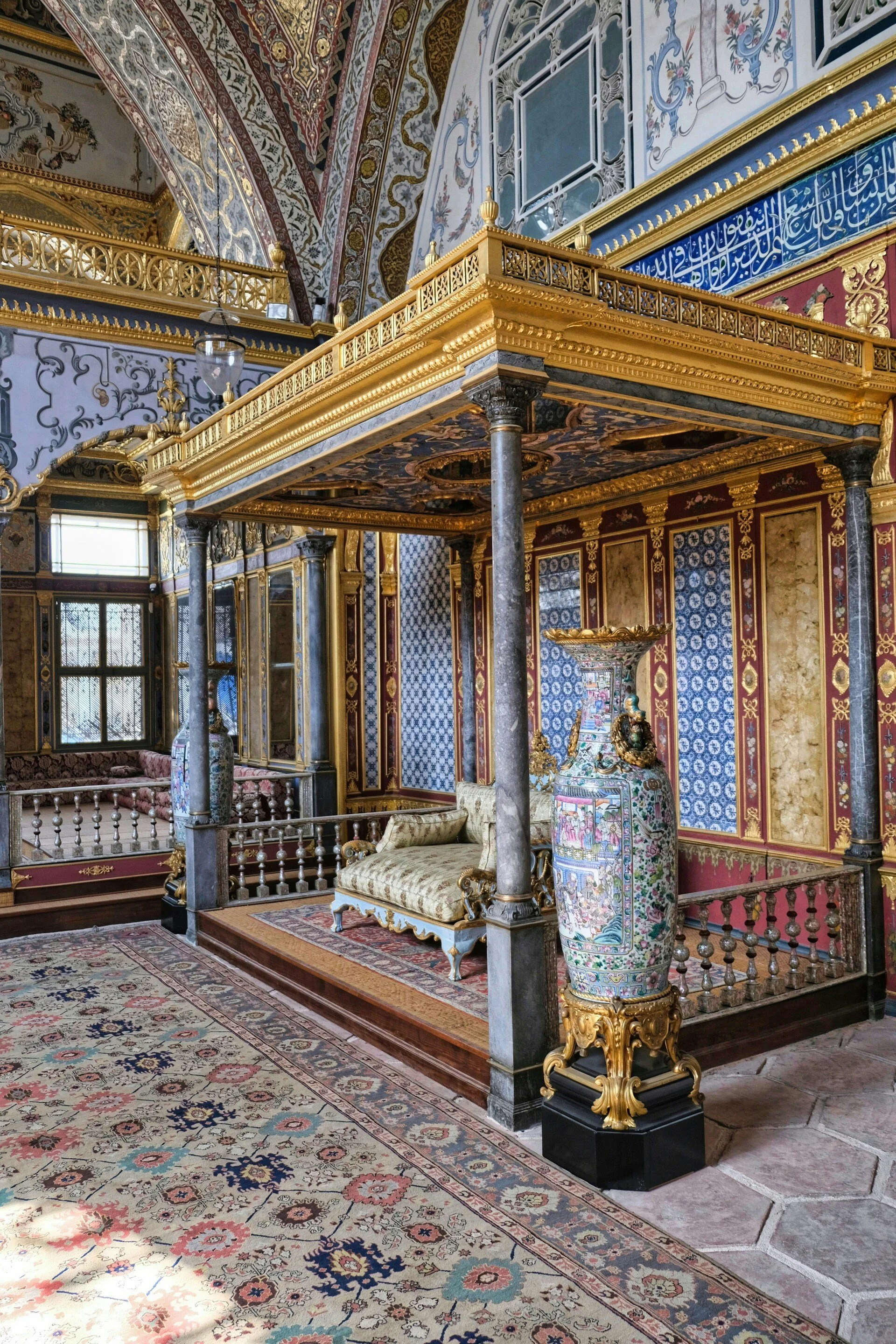 Decorative room with ornate furniture, gold accents, blue patterned walls, and Persian-style rug.