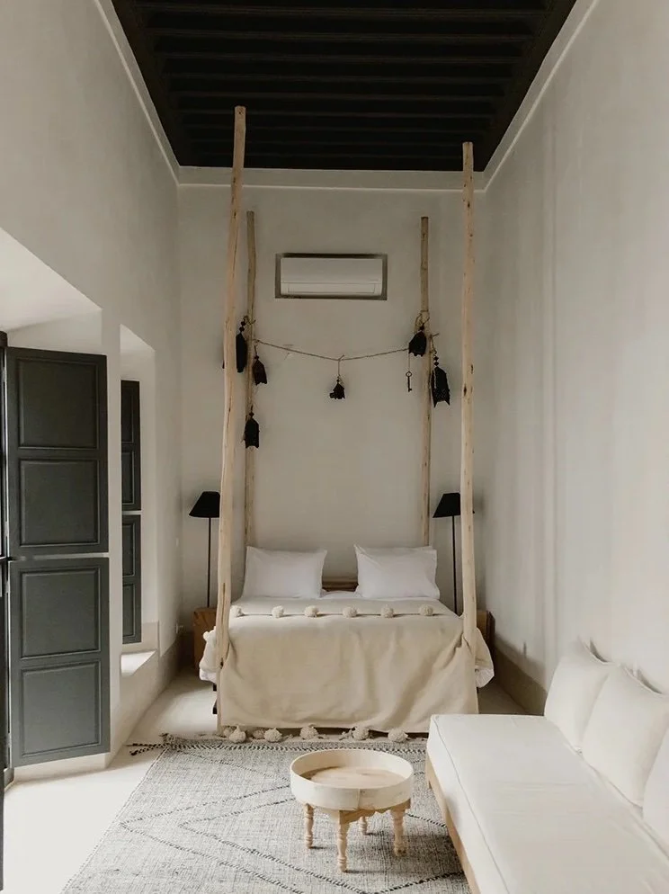 Elegant bedroom with twin beds, decorative wooden partition, cozy armchair, and window seat with blue cushions.