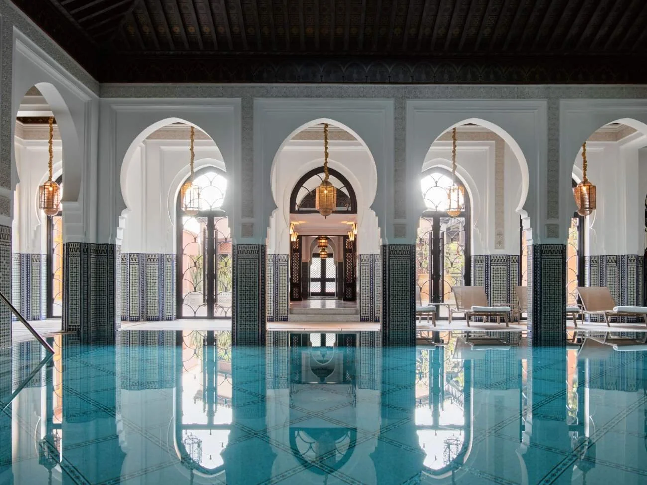 Interior view of a luxurious Moroccan-style indoor pool with arched columns and tiled walls.