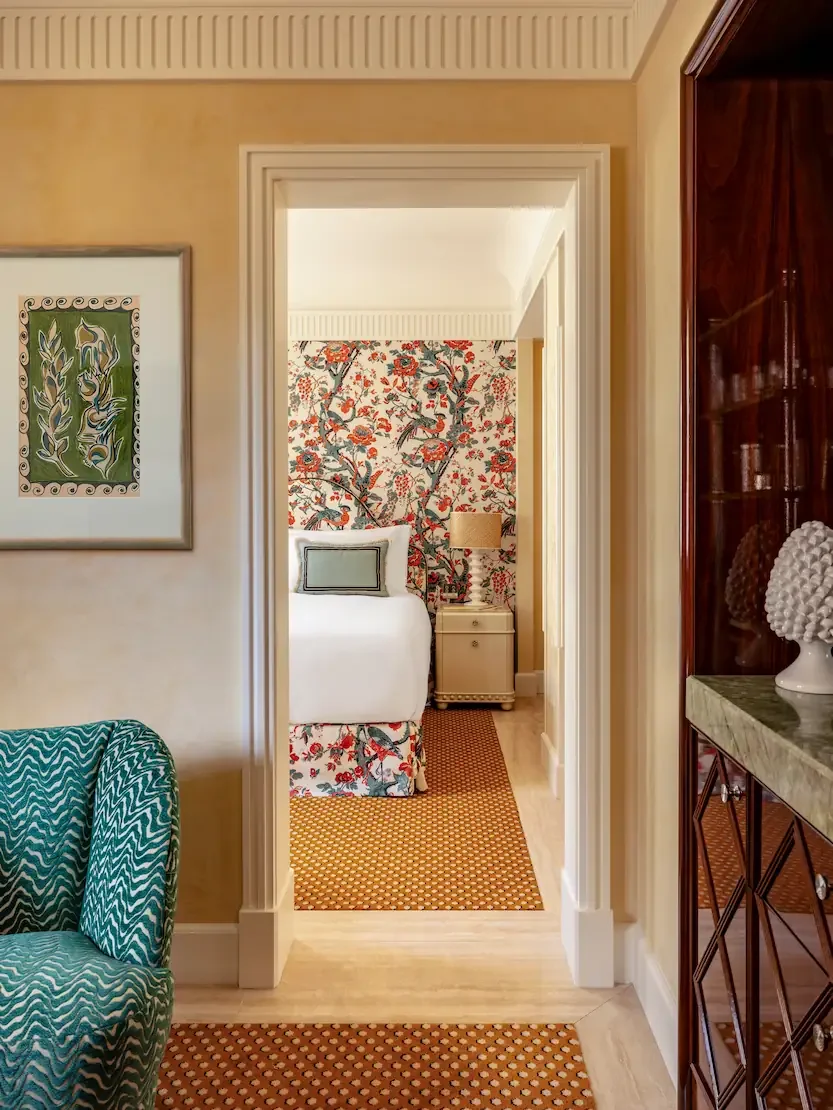 Hotel facade covered in green ivy and flowering plants, with a lit entrance and a tall spire in the background, against a purple evening sky.