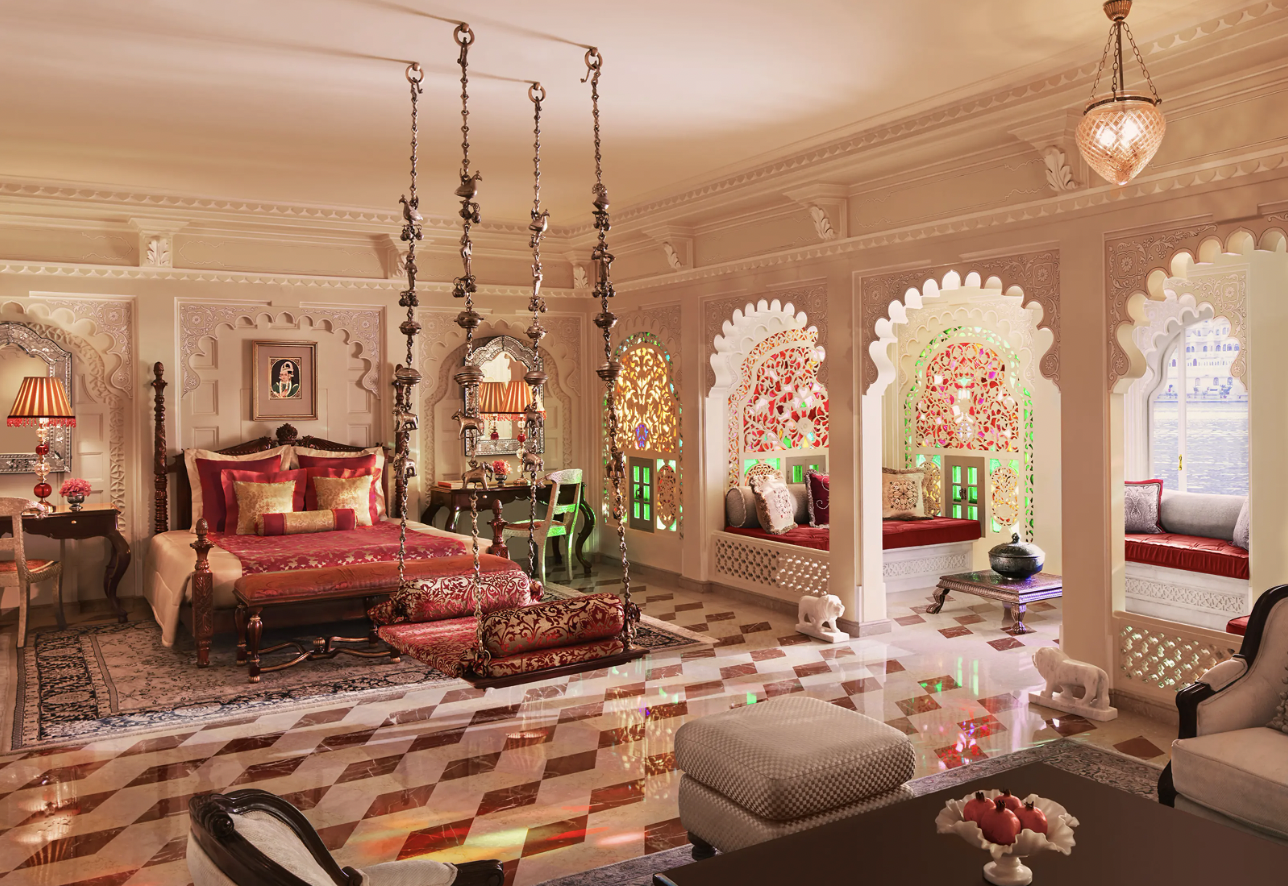 Luxurious room with ornate decor, featuring a large bed with red and gold accents, hanging swing, carved arches with stained glass, and plush seating areas.