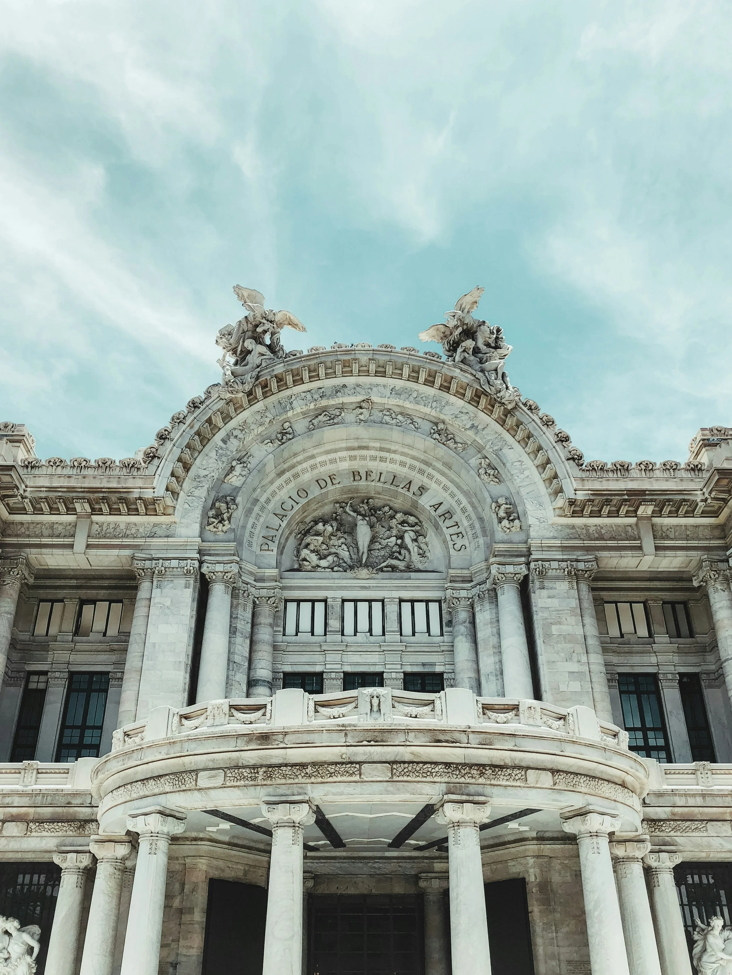 Front view of Palacio de Bellas Artes with intricate architectural details and sculptures under a blue sky.