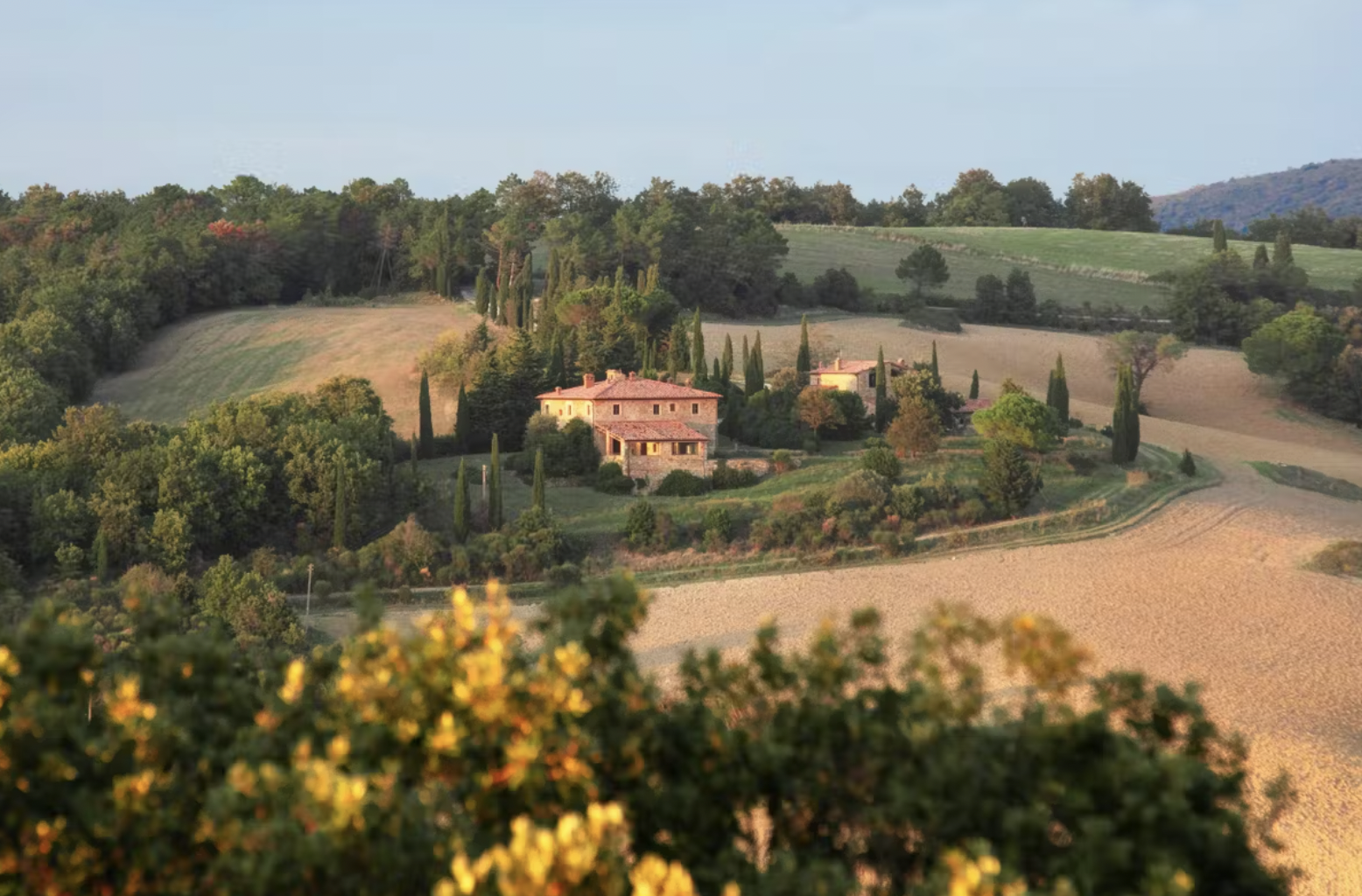 Italian countryside with a villa, surrounded by fields and trees, under a clear sky.