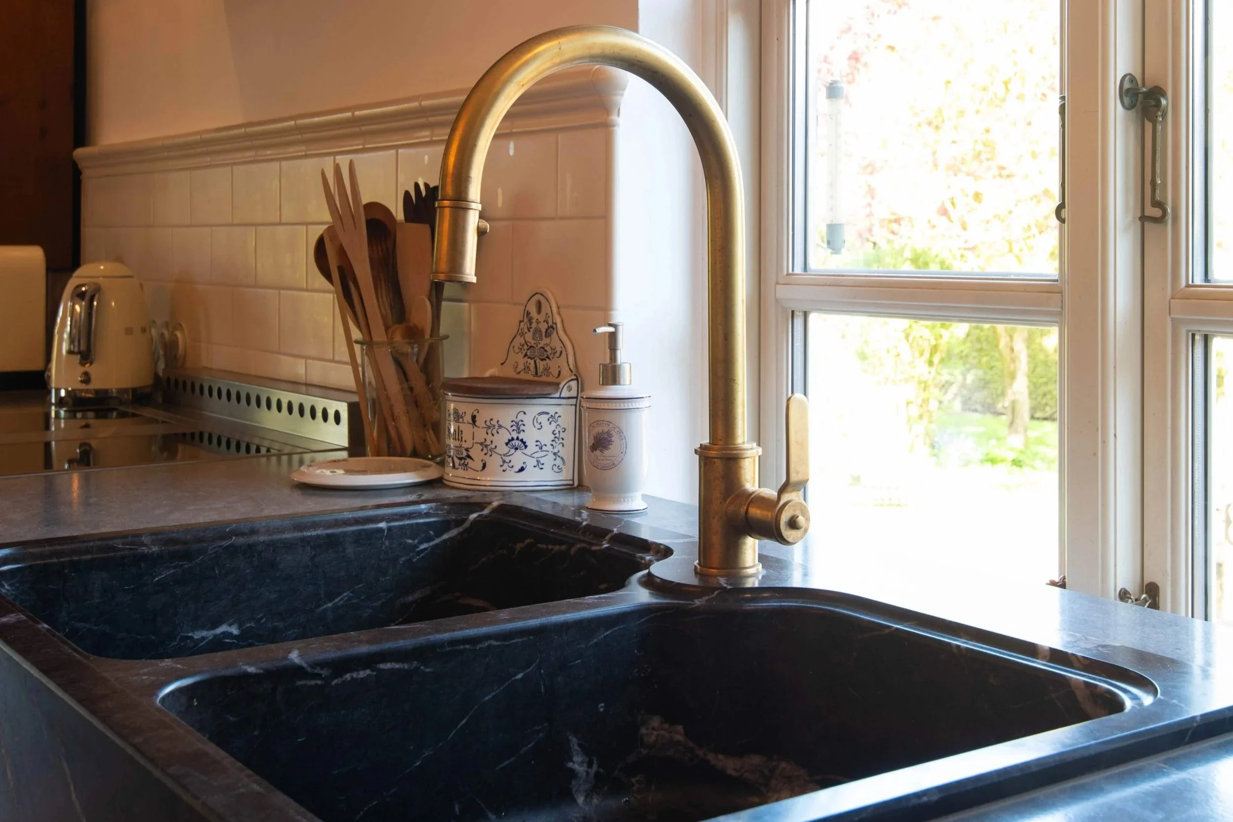 Blick auf eine Küchenspüle aus schwarzem Marmor mit grauer Granit-Arbeitsplatte und einem messingfarbenen Wasserhahn.