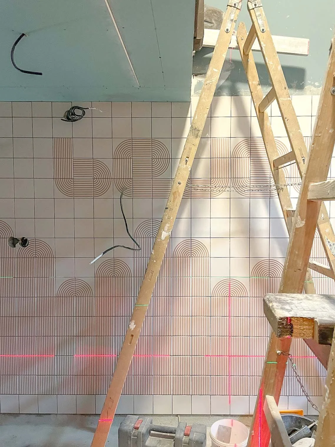 Construction site showing a tiled wall with geometric patterns, electrical wiring, and a wooden ladder.