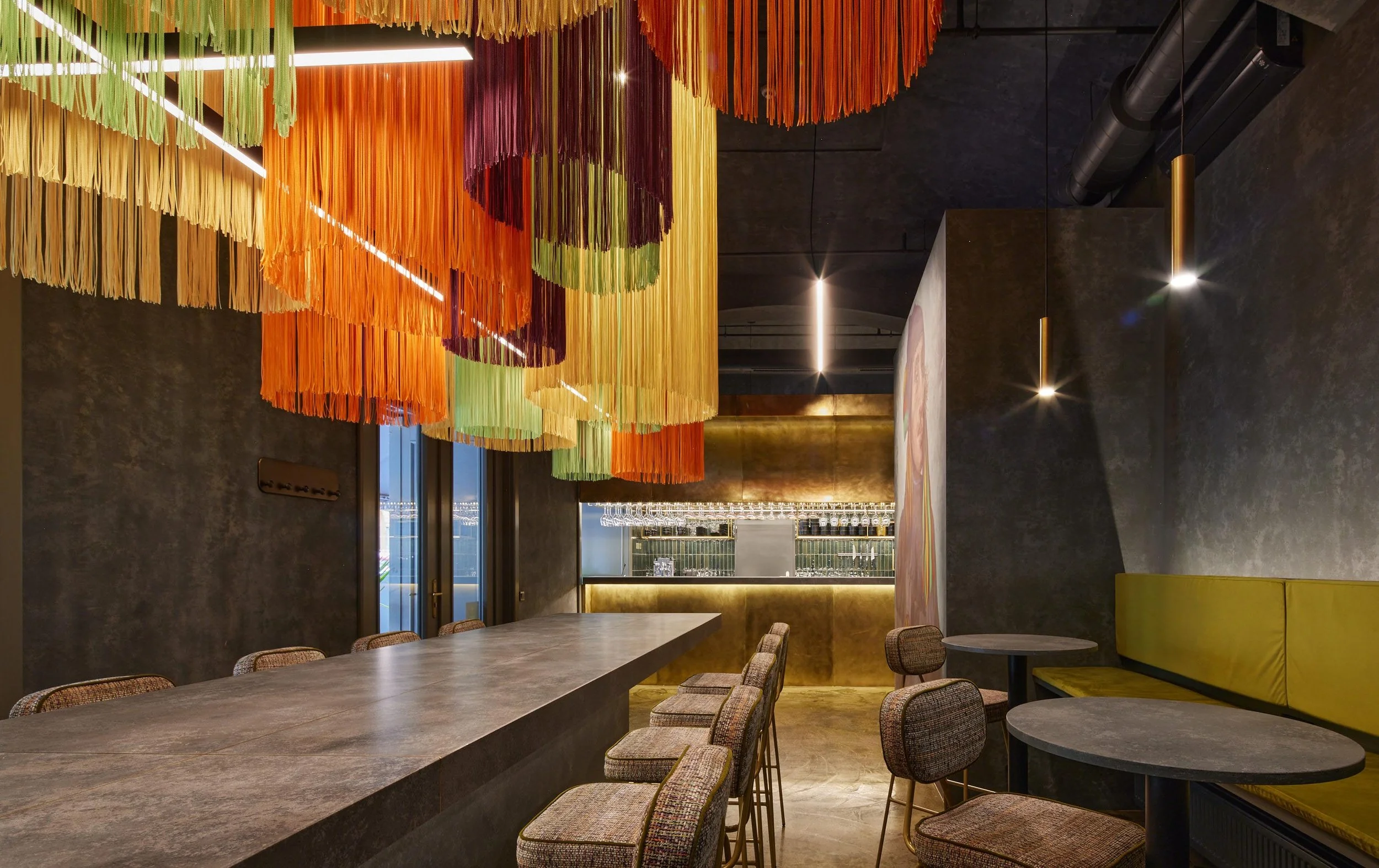 Interior of a modern restaurant with colorful hanging decorations, a long bar counter, and seating areas.