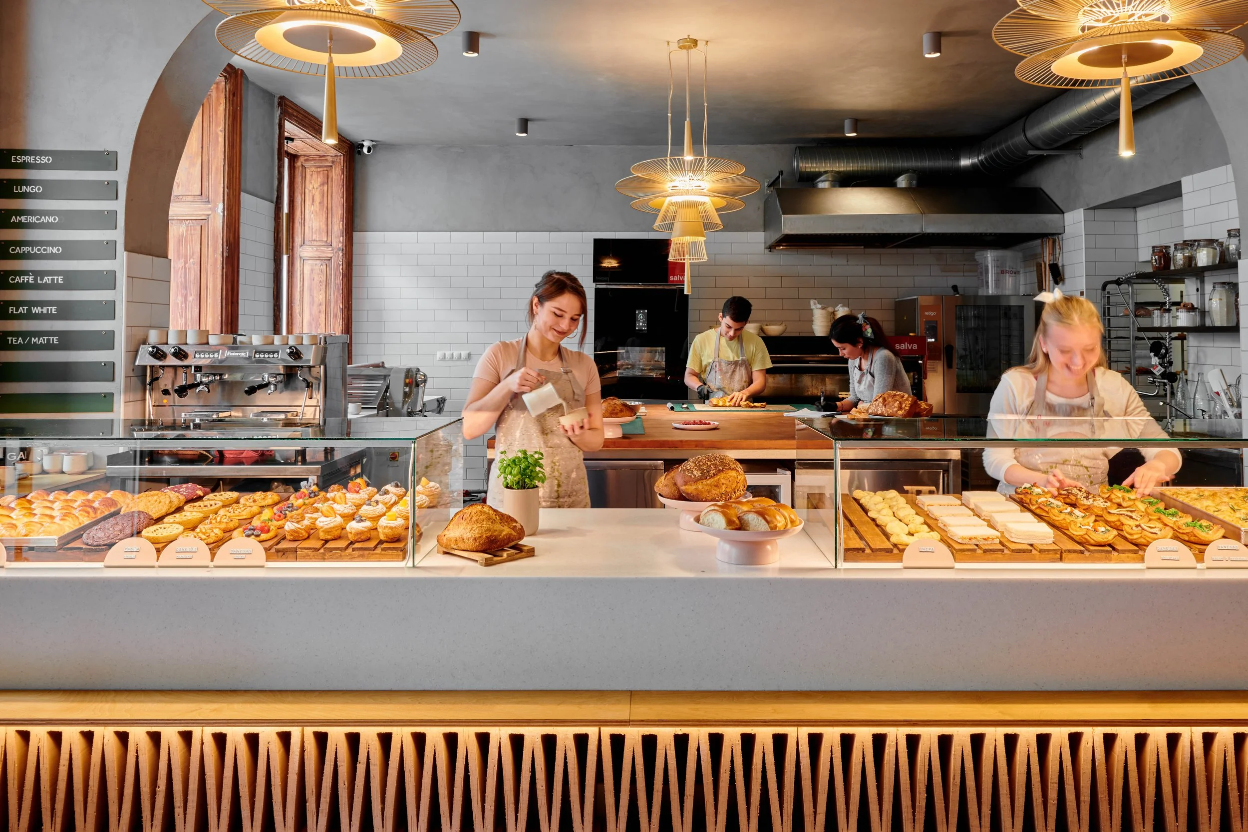 A bakery counter with a variety of baked goods and four employees preparing and arranging pastries inside a modern coffee shop.
