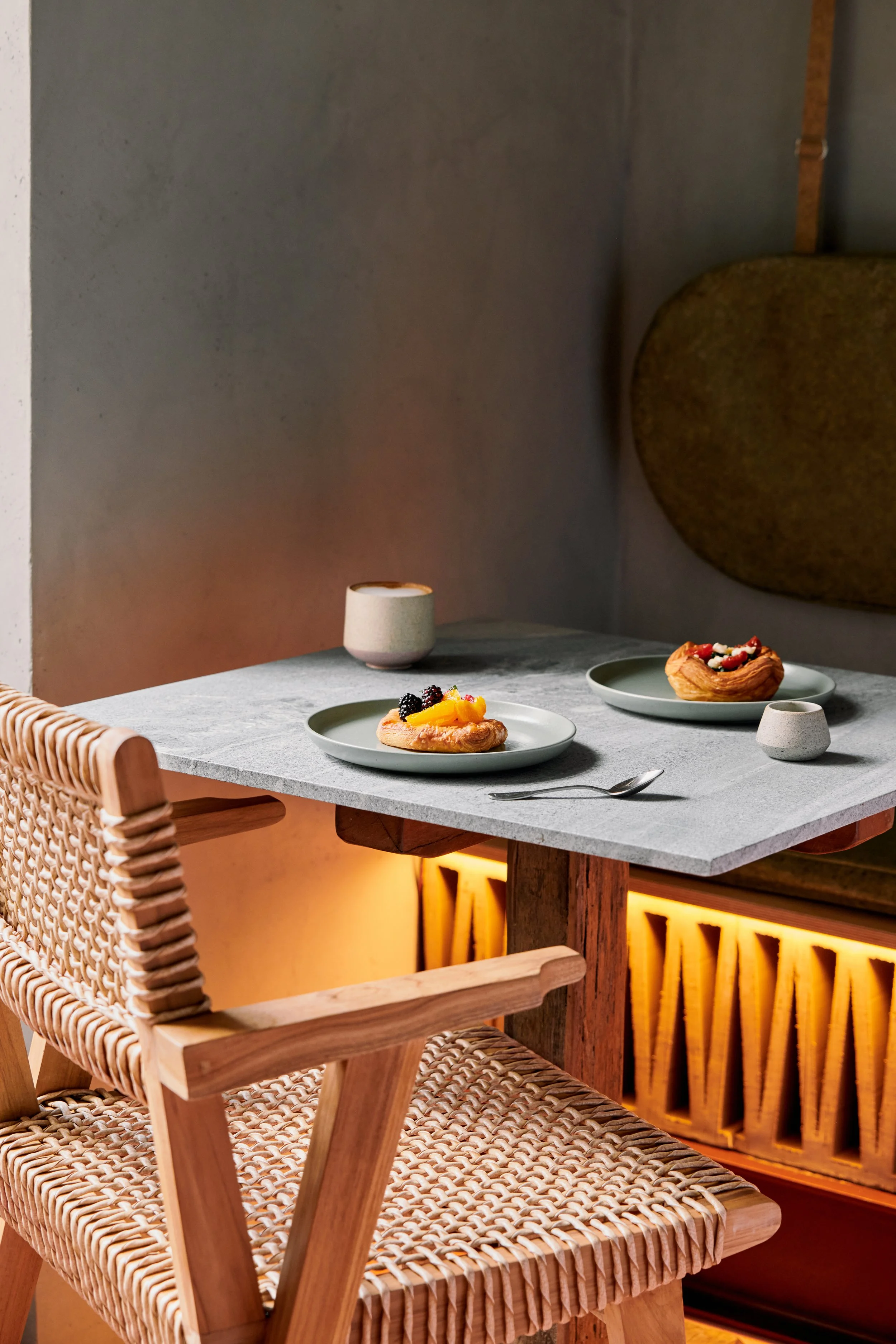 A dining table with two plates of dessert, a spoon, and two cups, in a modern, cozy restaurant setting.