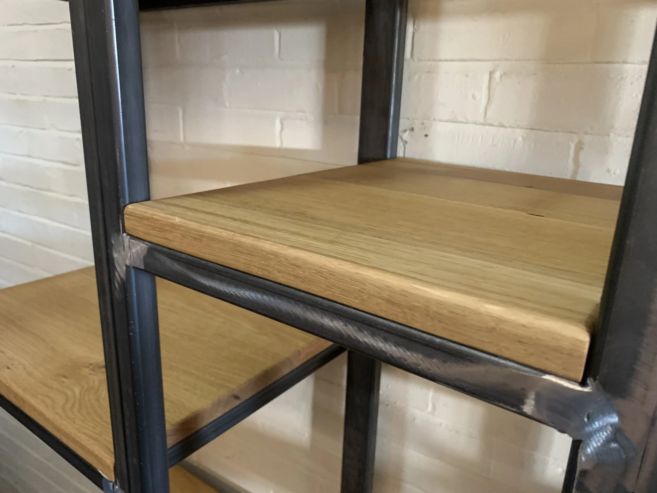 Industrial metal‑frame shelving unit with light hardwood shelves against a white brick wall.
