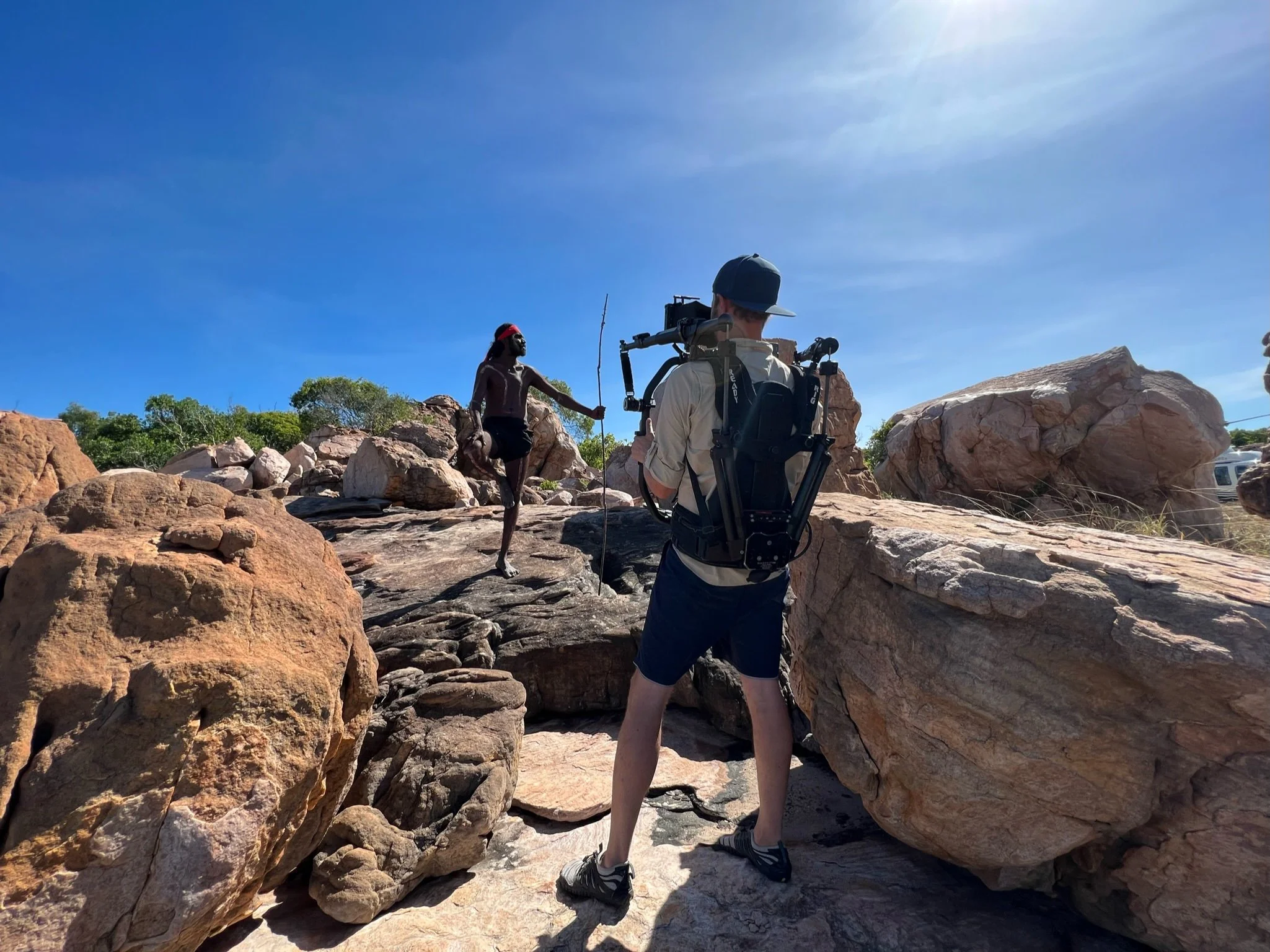 Filmmaker filming a person hiking on rocky terrain against a bright blue sky in Kimberley Australia. 