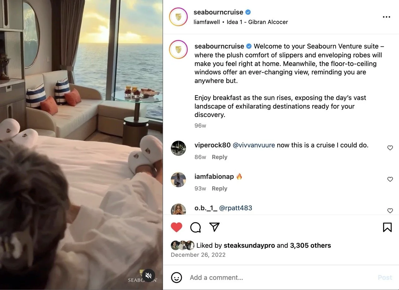 View from Seabourn Venture Panorama Suite showing a bed, slippers, a sofa with pillows, and a large window with a view of the ocean and sunset. WABU Creative, Scott David Martin