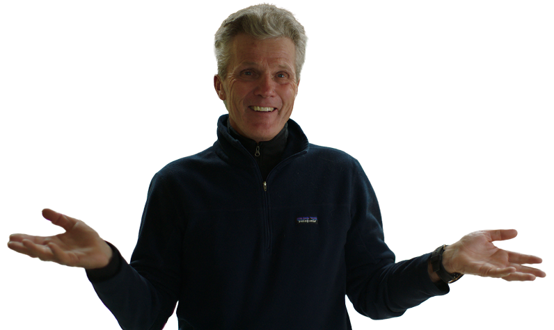 A smiling Alaskan man with gray hair wearing a dark zip-up jacket, with arms outstretched and palms facing up in a questioning or shrugging gesture.