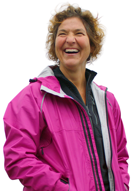 An Alaskan woman smiling woman with curly hair wearing a pink jacket and black shirt.