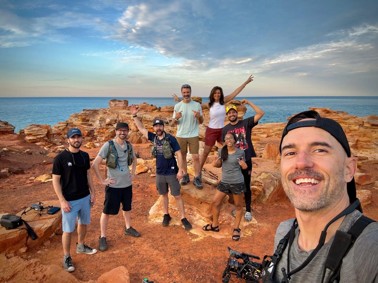 Kimberley Australia Cruise. Group of eight friends taking a selfie on rocky coast with ocean and sky in the background.