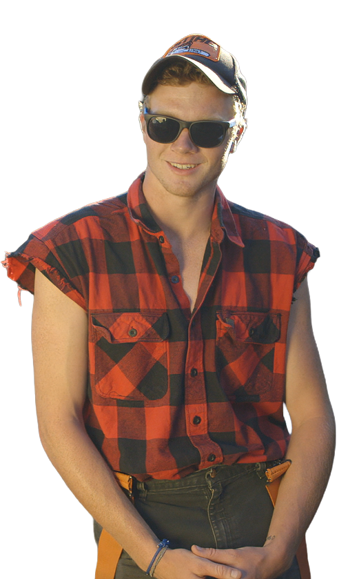 An Alaska lumberjack wearing sunglasses, a baseball cap, and a red and black plaid sleeveless shirt smiling outdoors.