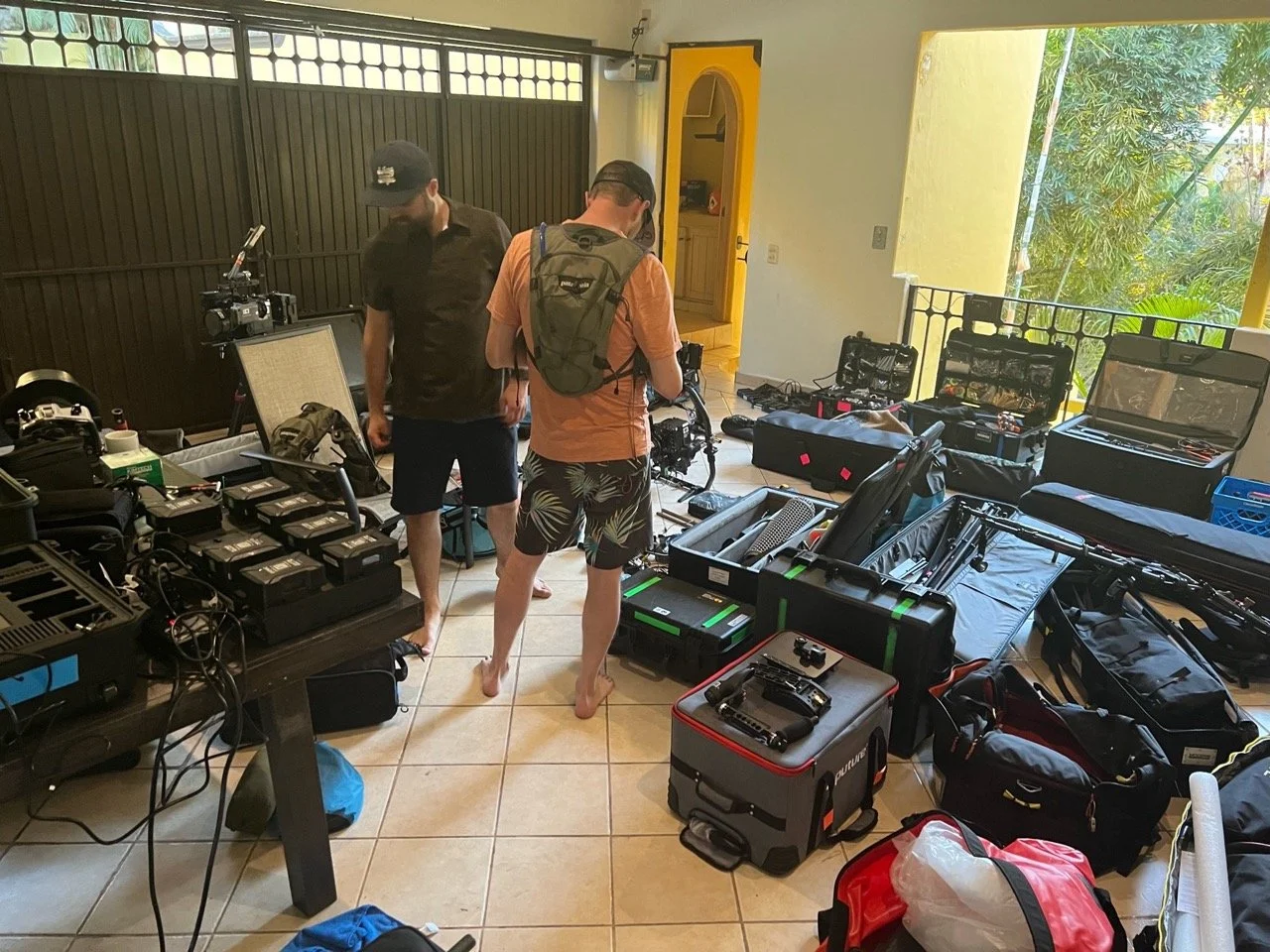 Behind the Scenes of WABU Creative. Production Manager Andrew Wright & Director Scott David Martin are preparing camera equipment with various cases and gear laid out on the floor in Puerto Vallarta, Mexico. 