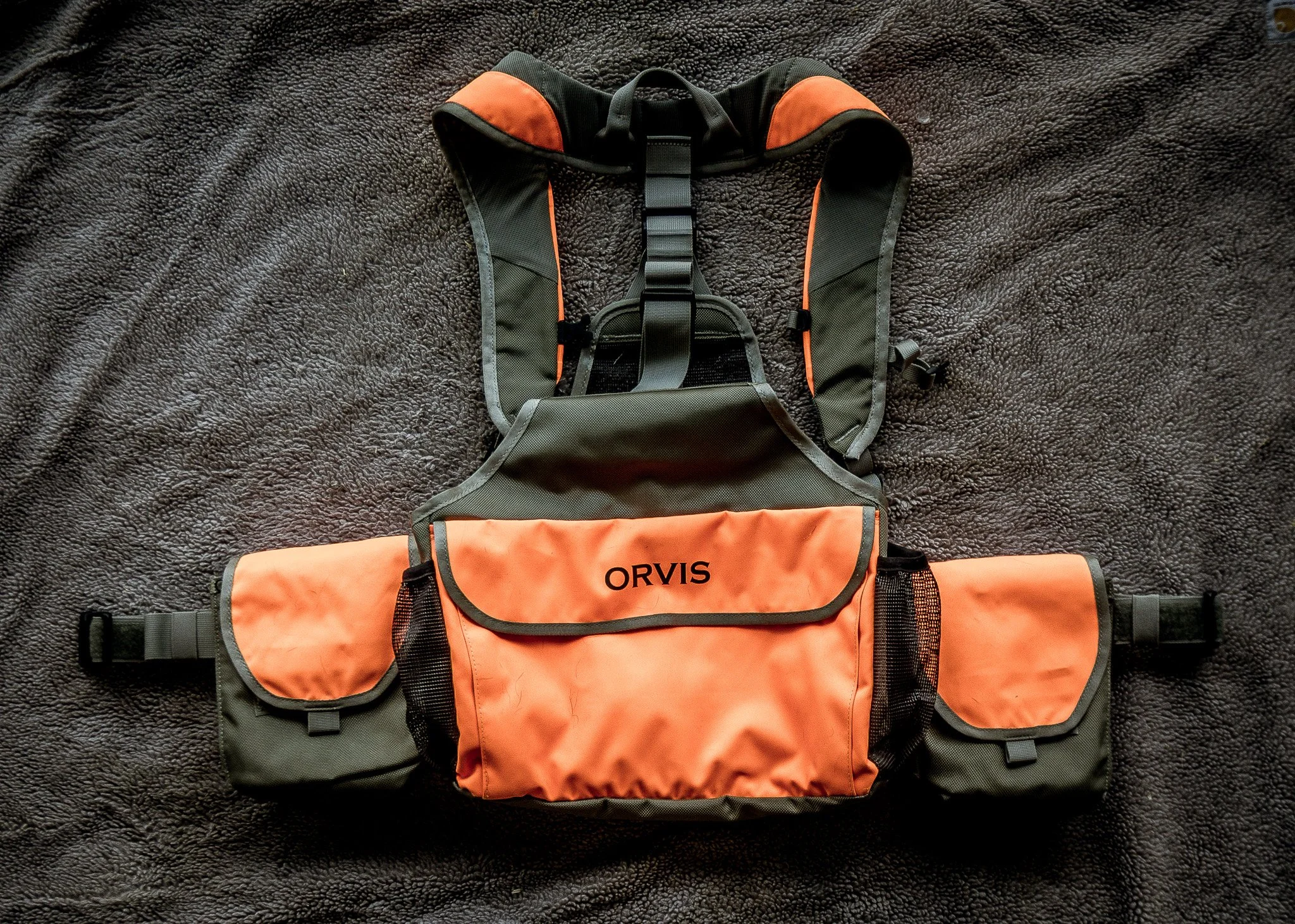 A black and orange Orvis fishing waist pack laying on a dark textured surface.