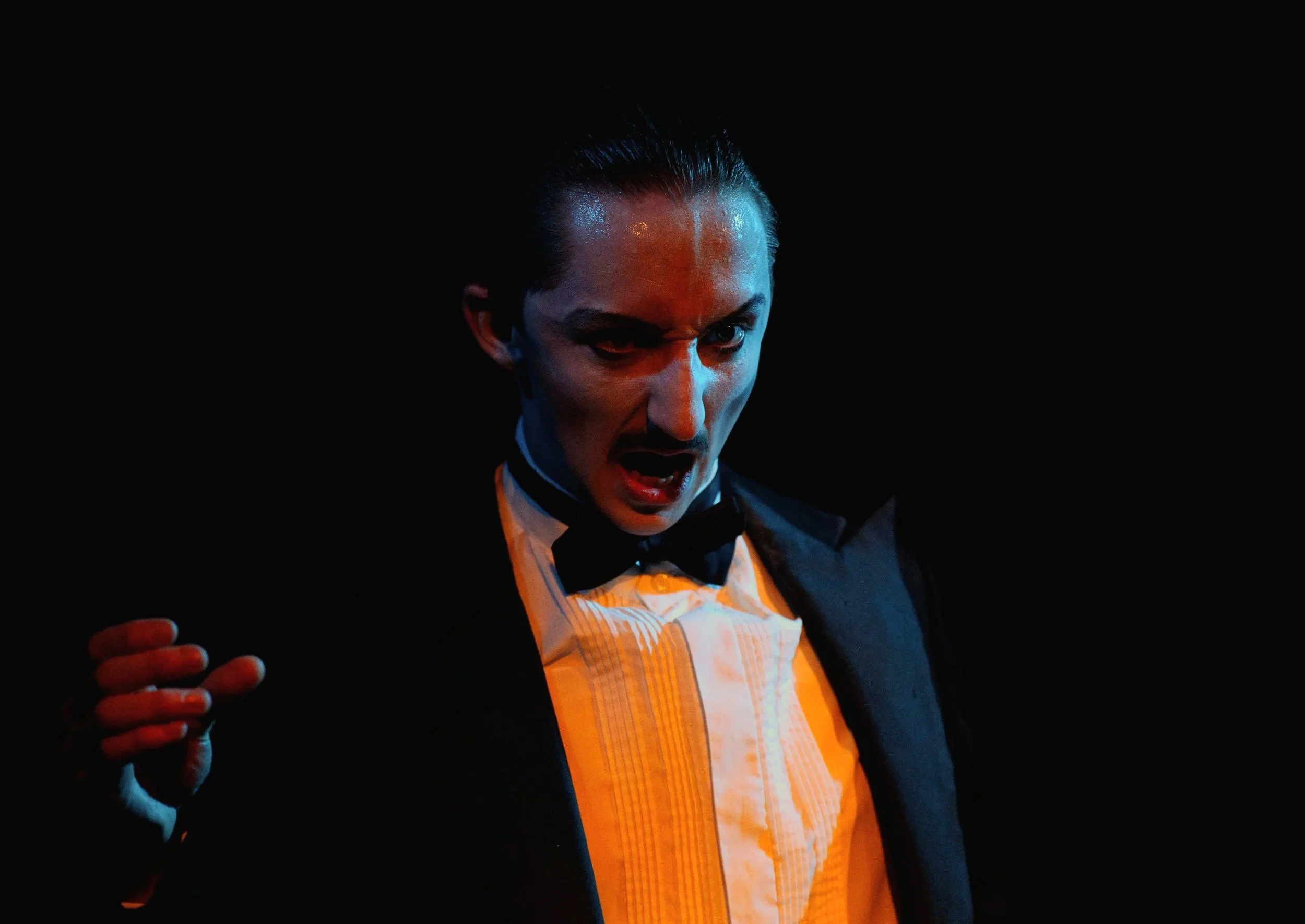 Man dressed in formal tuxedo with a bowtie, expressing an intense or angry emotion, with dramatic lighting and a dark background.