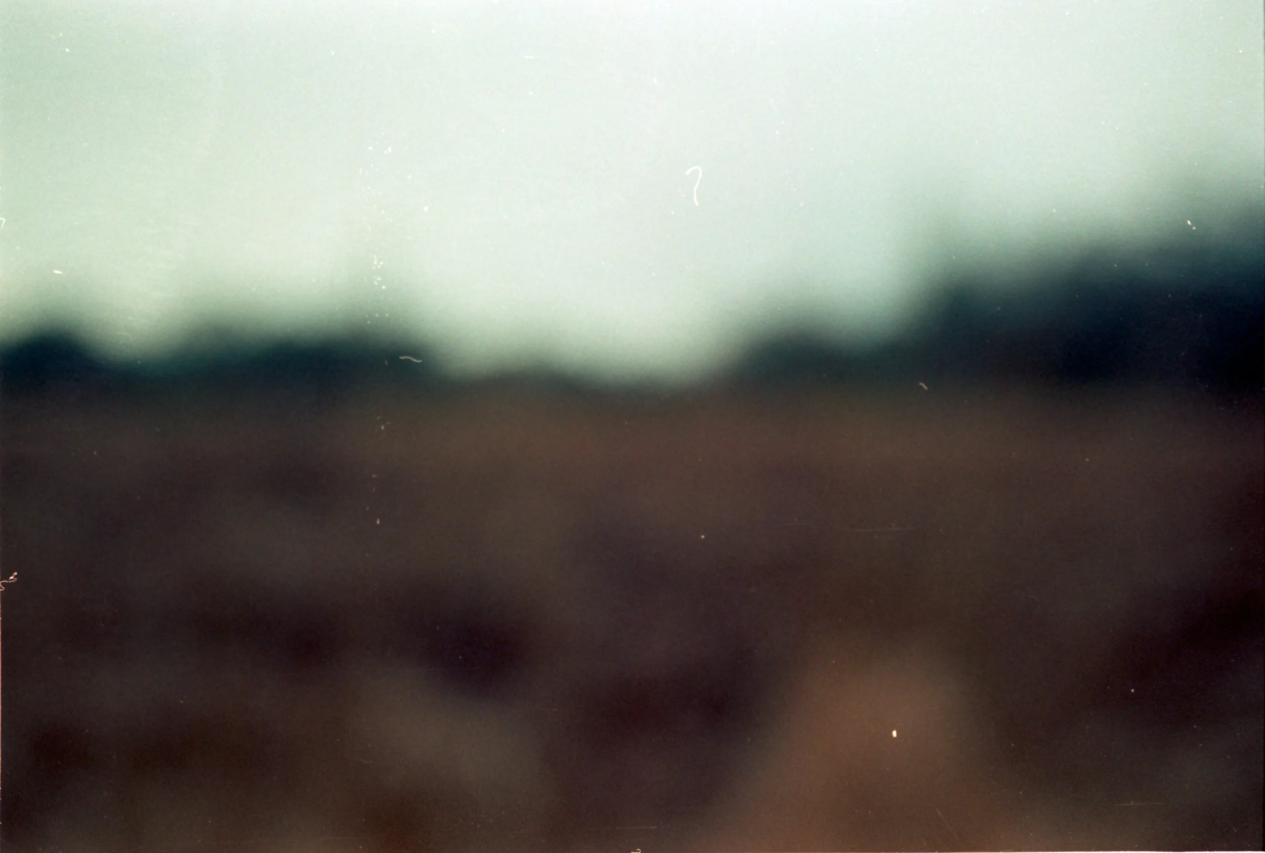 A blurry landscape image showing an overcast sky with a horizon line, possibly of land or fields, with no distinct objects or features visible.