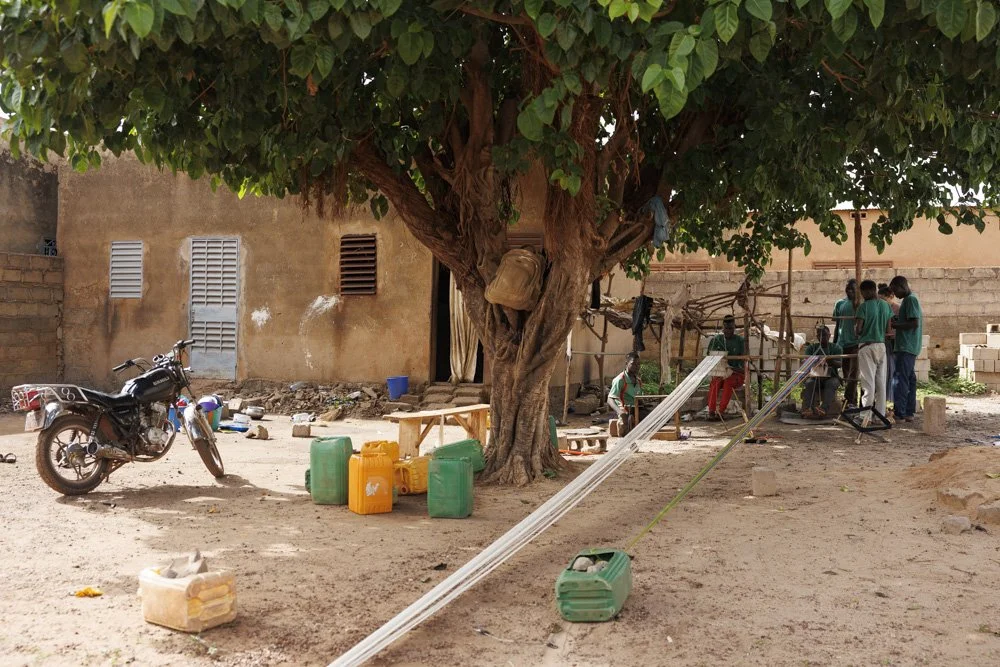 A group of internally displaced persons weave yarn to craft accessories under a tree in a compound where they live, Bobo Dioulasso, Burkina Faso. They fled their villages due to terrorist attacks.