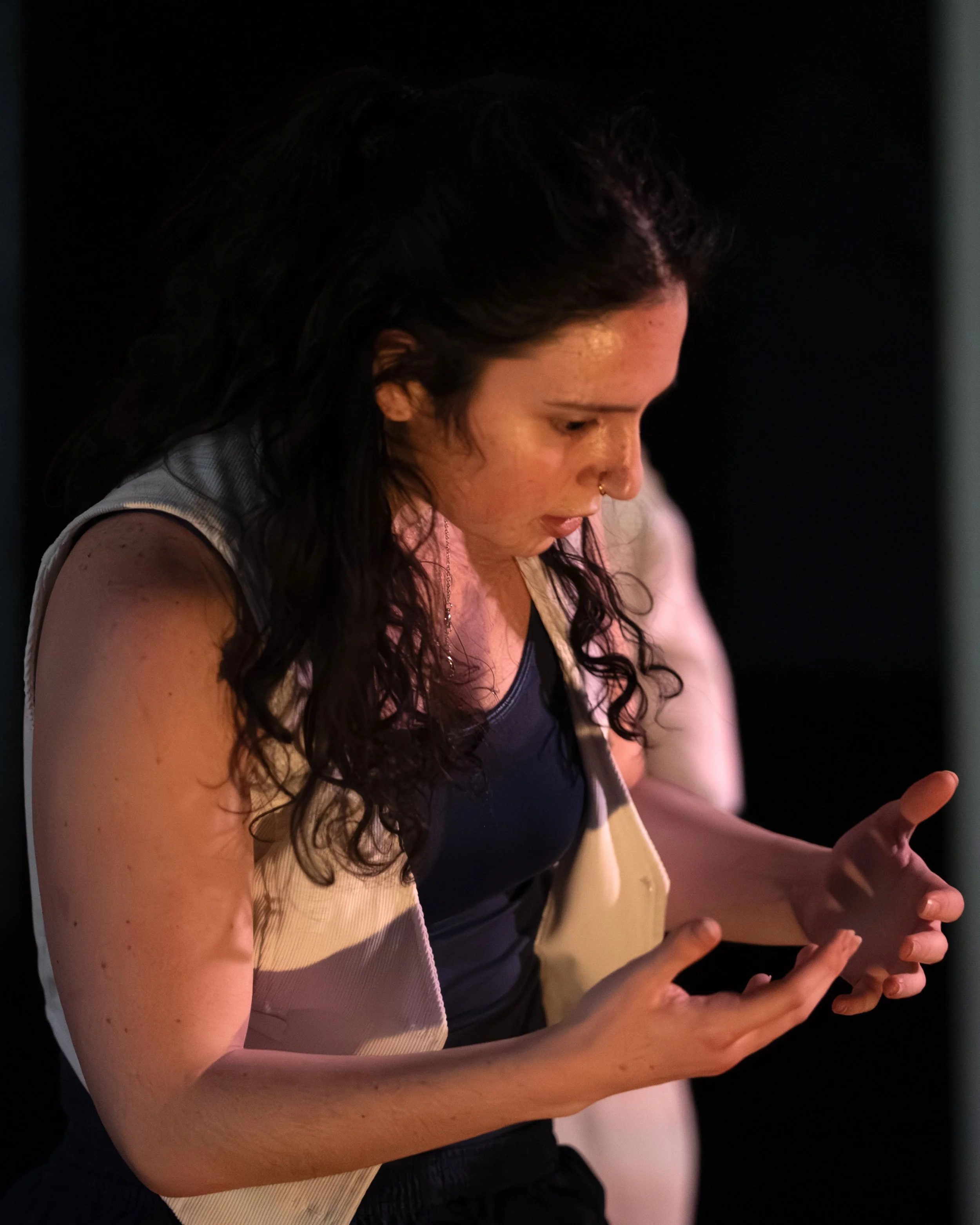 Young woman with dark curly hair looking at her hands with a concerned or focused expression.