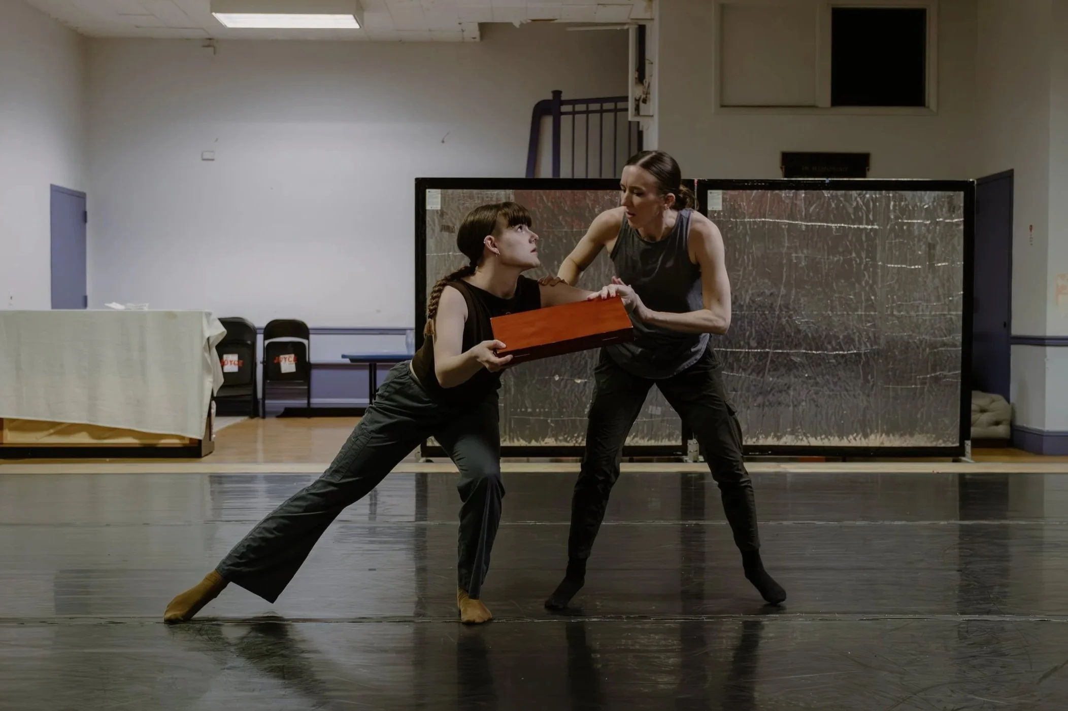 Two dancers in a studio, one holding a brown, wooden briefcase. They are struggling over the briefcase, as if only one of them can hold it.