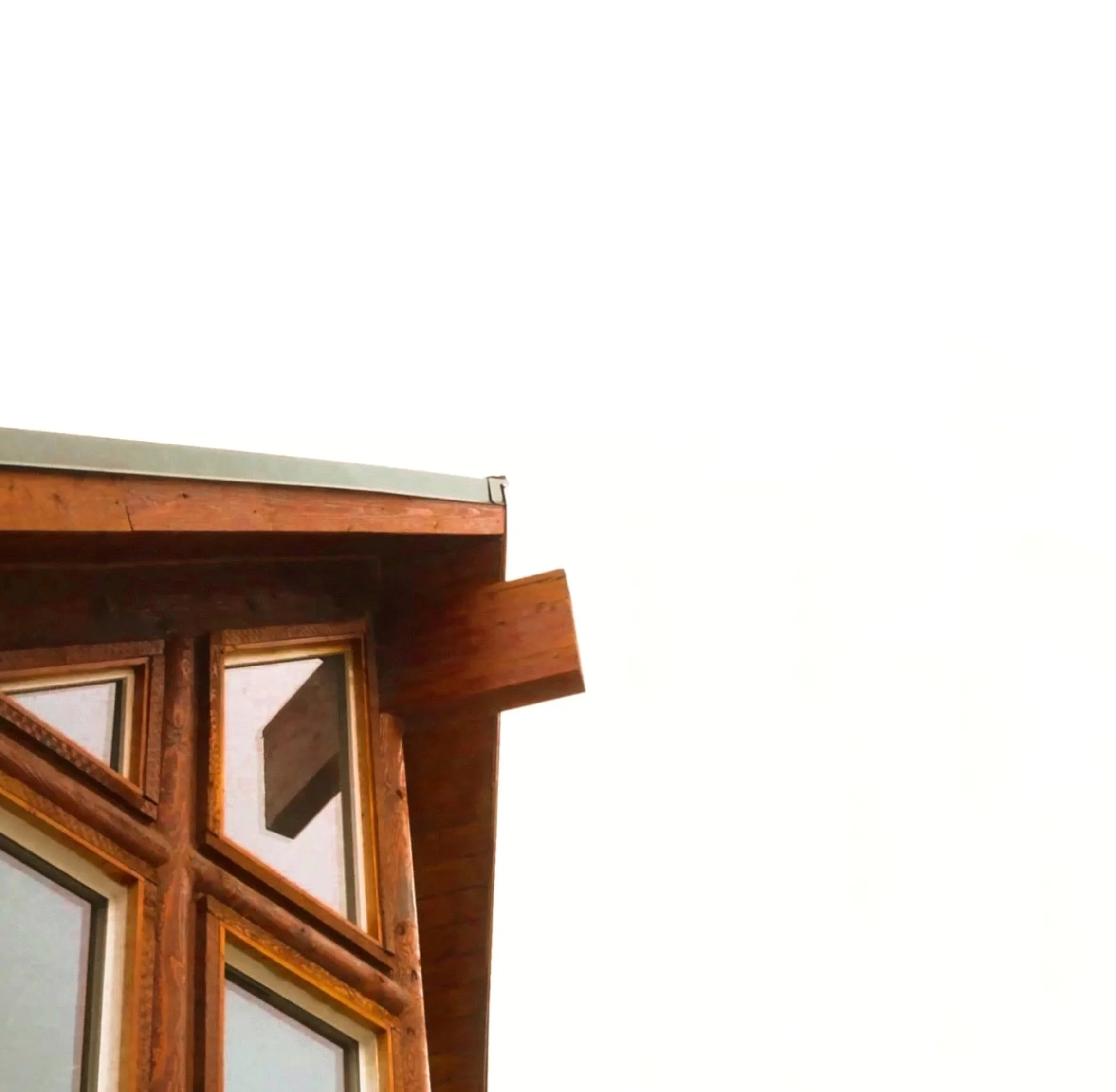 Close-up of a wooden house exterior with windows and a roof, against a cloudy sky.