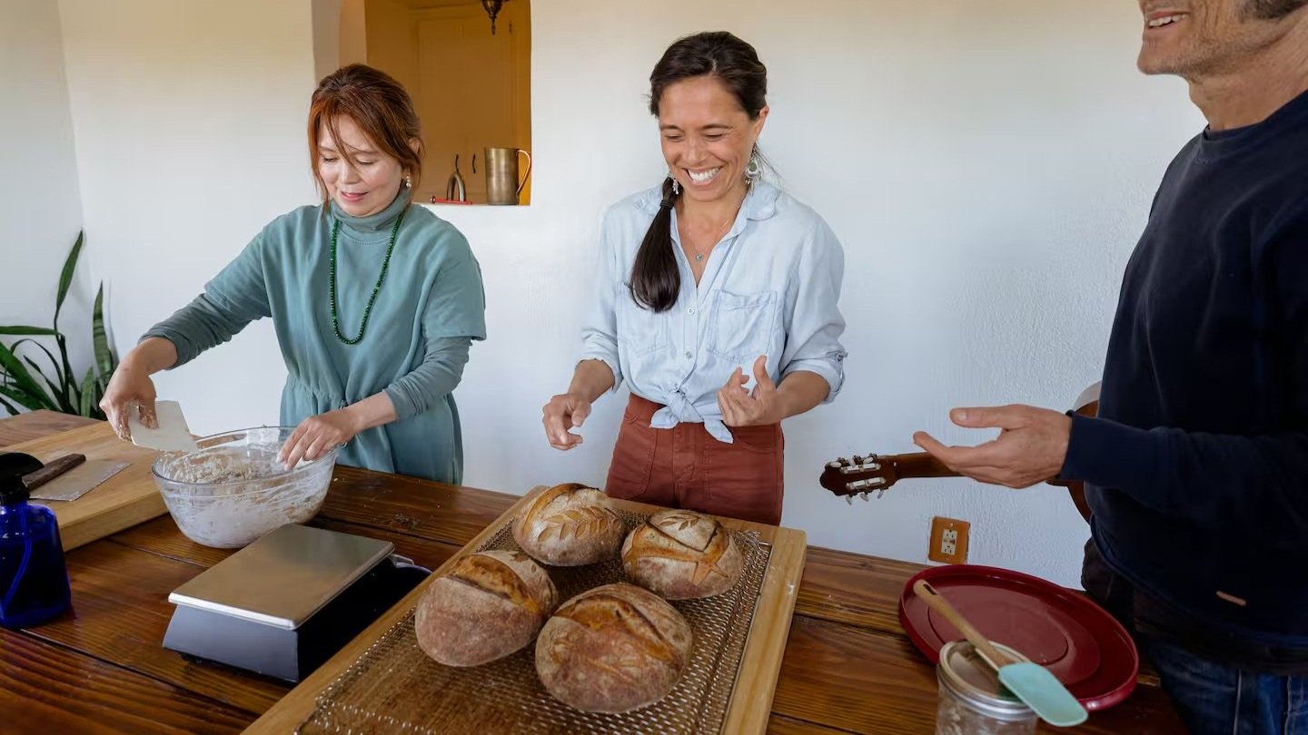 Three people baking bread together in a kitchen, smiling and enjoying the activity.