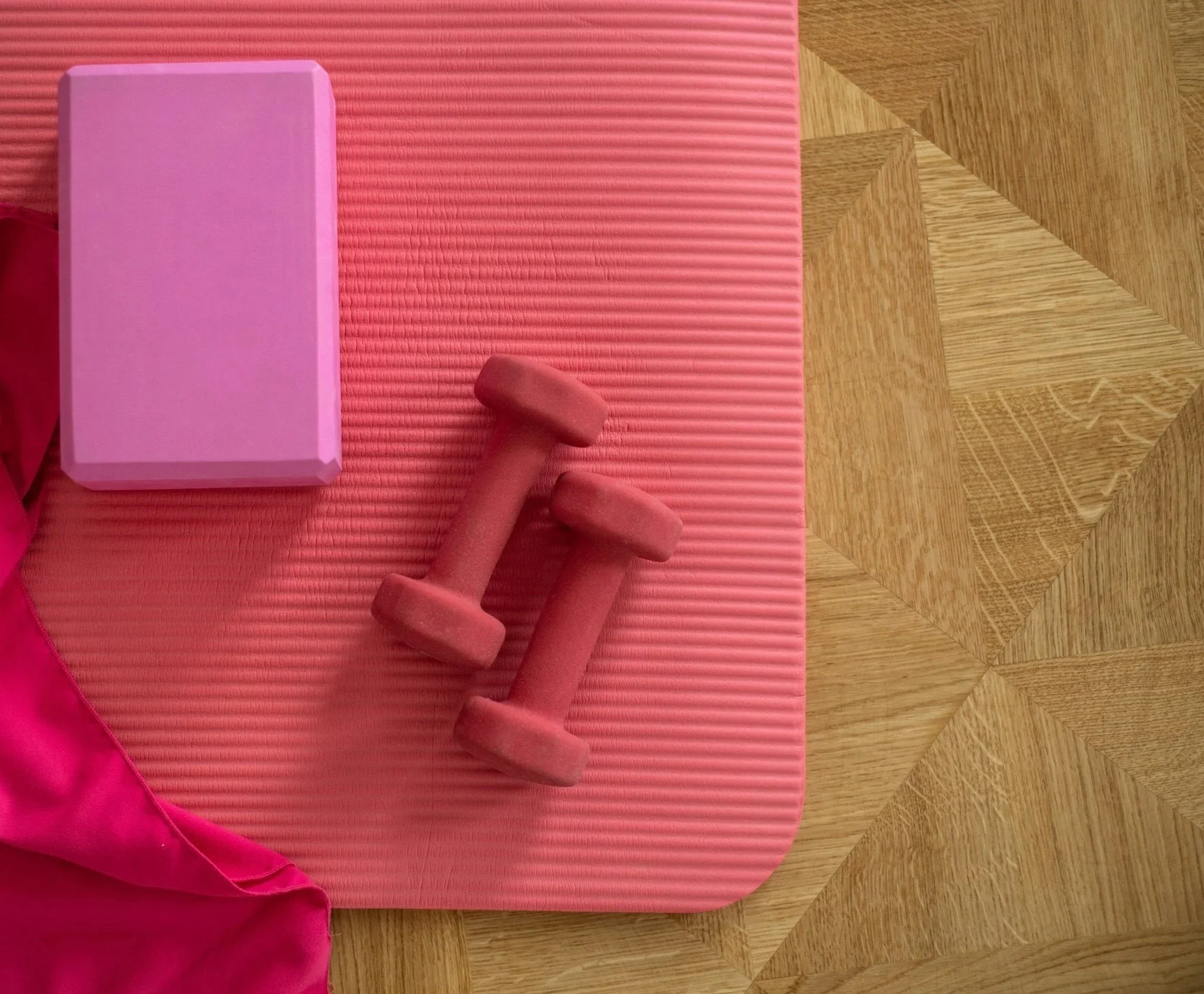 A pink gym mat on a wooden floor with a foam roller and a person's hand holding one of the foam roller's ends.