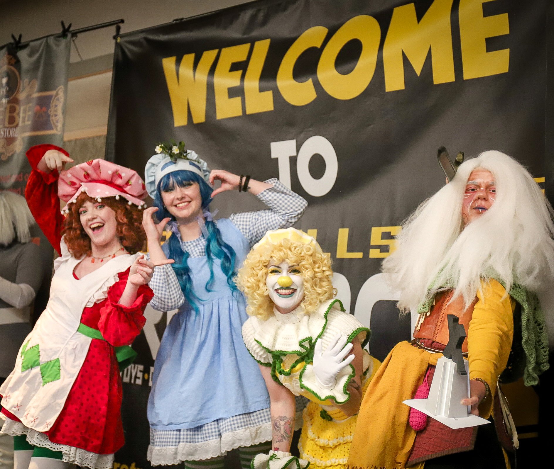 Image shows eight participants in comic con event. They're dressed in costumes and are posing for the camera.