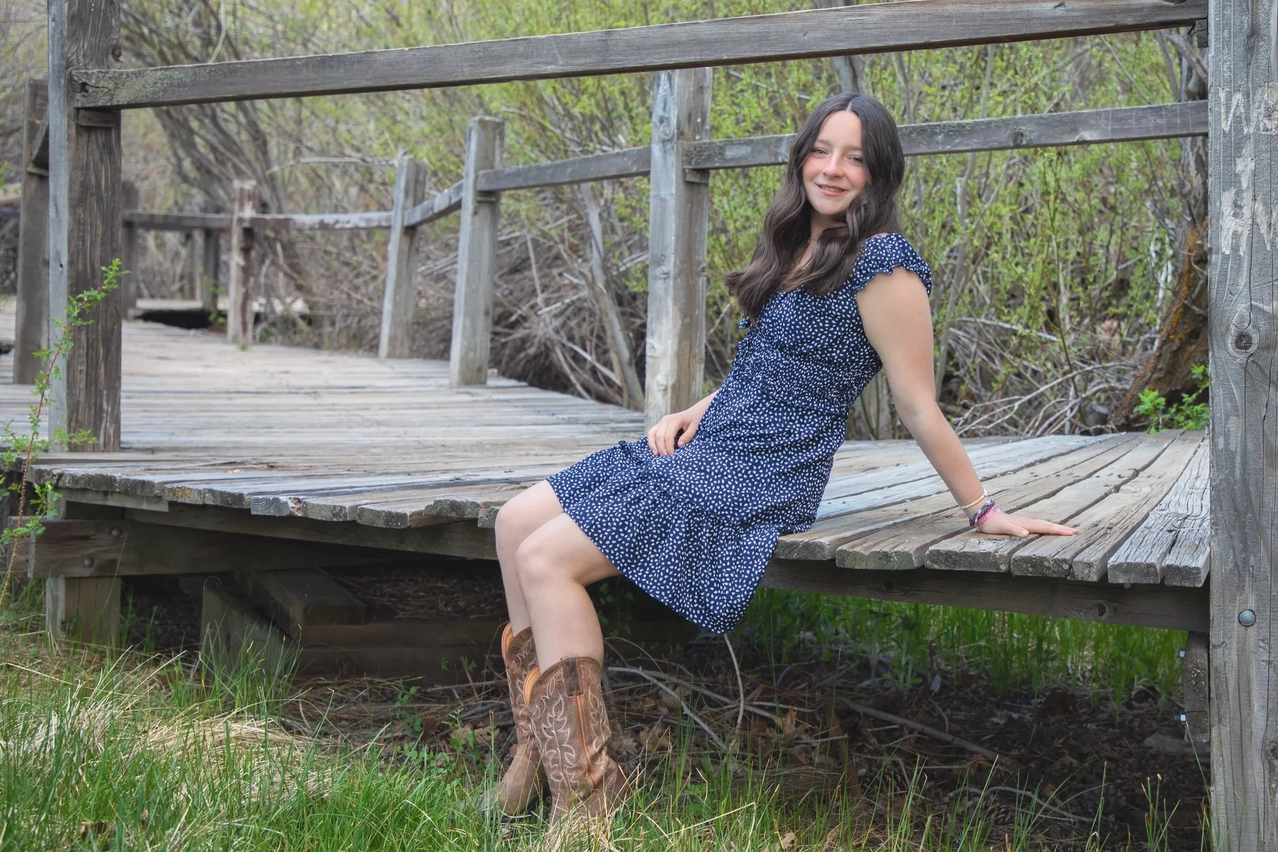 A young girl sitting and leaning back on her hand on a wooden bridge surrounded by greenery in Wrightwood by family photographer.