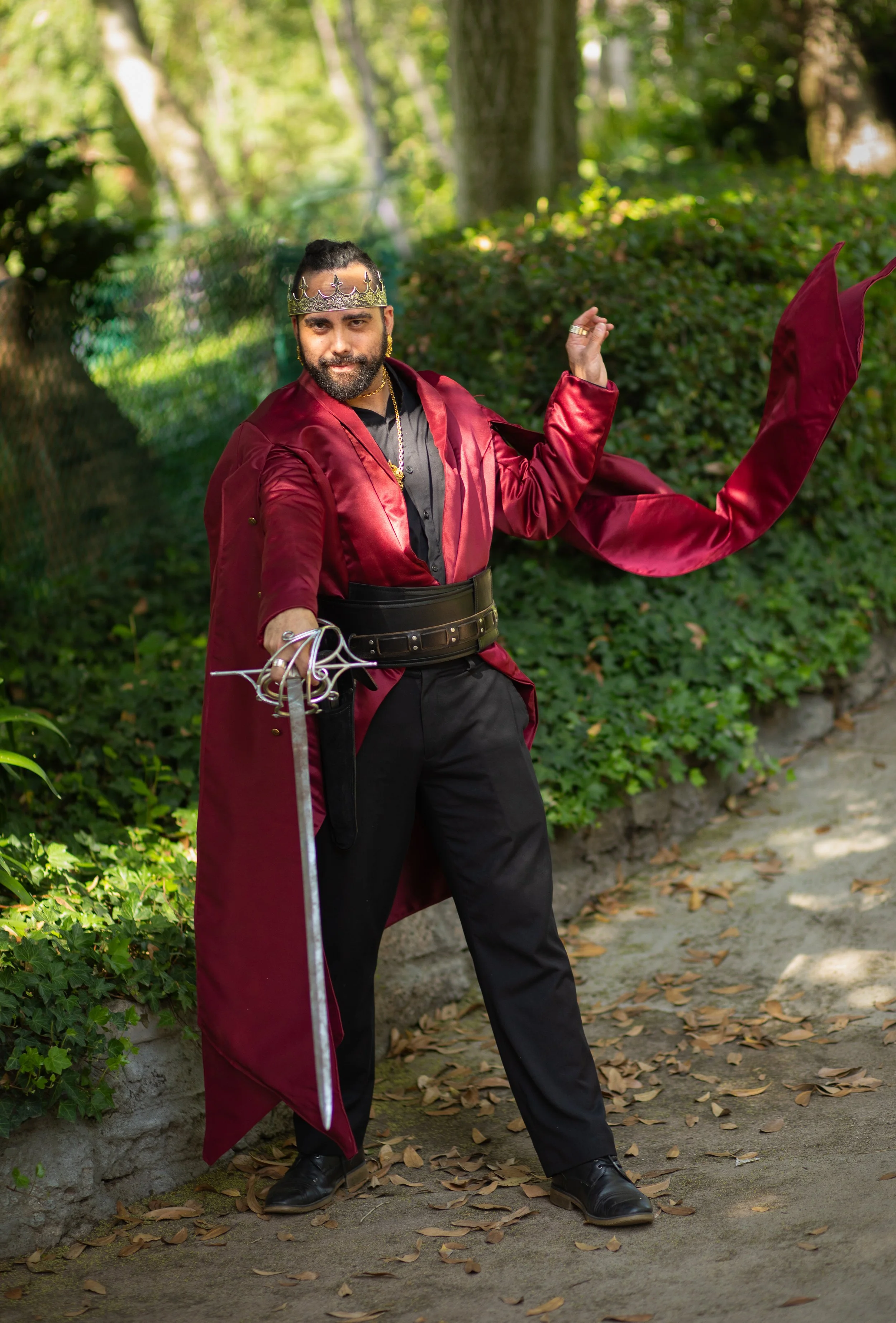 Southern california fantasy photographer took photo of man holding cape and sword outdoors in a park, while wearing a crown.