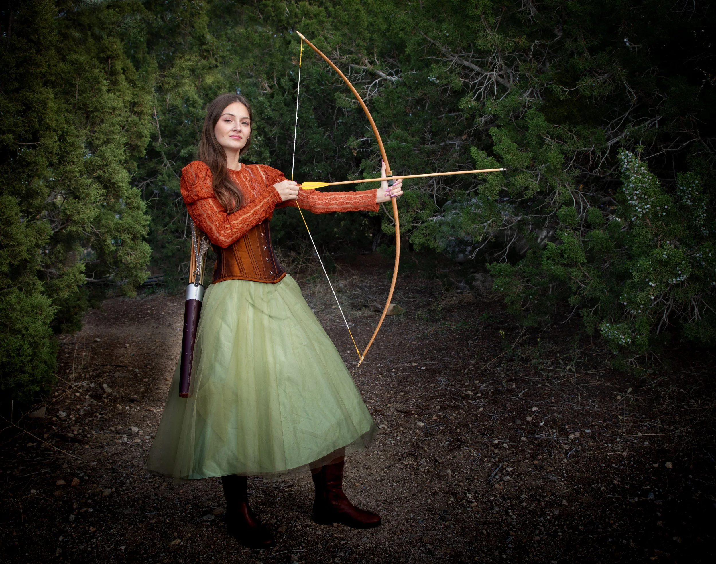 Enchanted forest portraits in the high desert by annette marie photography. girl wearing green skirt and orange corset holding vintage bow and arrows, standing in the juniper forest.