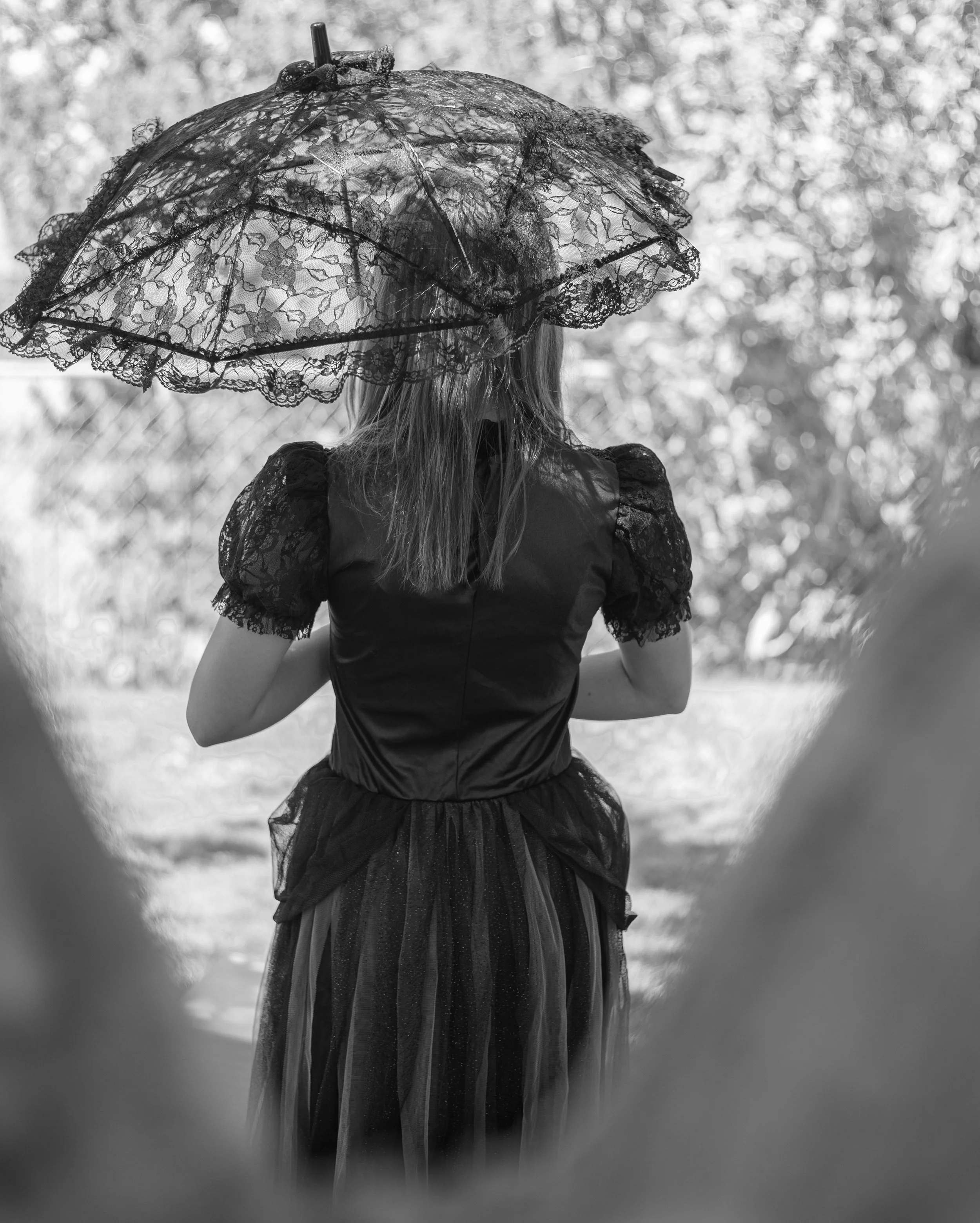 Girl wearing victorian dress, holding lace umbrella with back to camera by dark fairy portrait photographer.