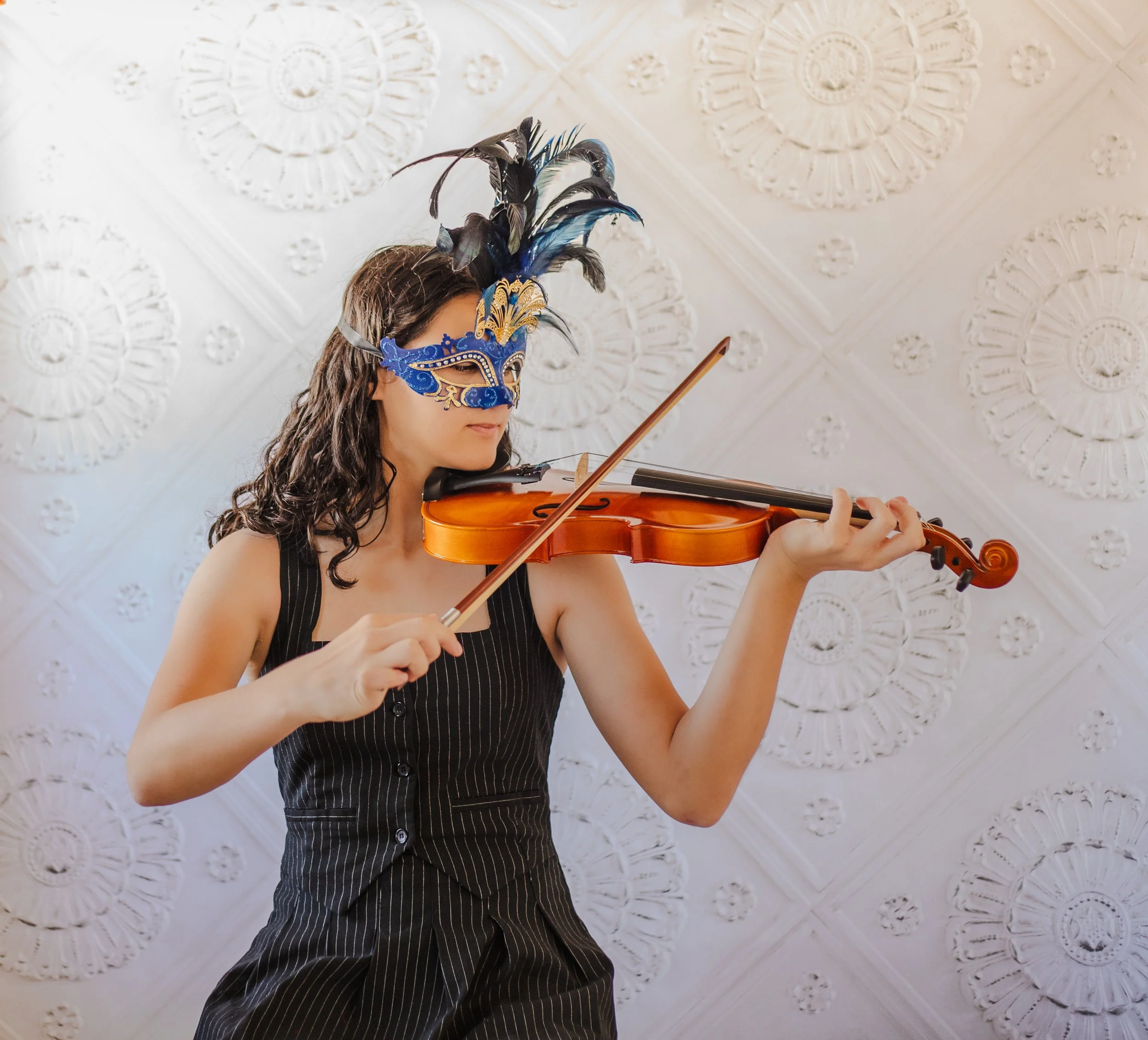 Senior playing violin wearing masquearde mask with a marquis backdrop. Fantasy studio photos in Fontana
