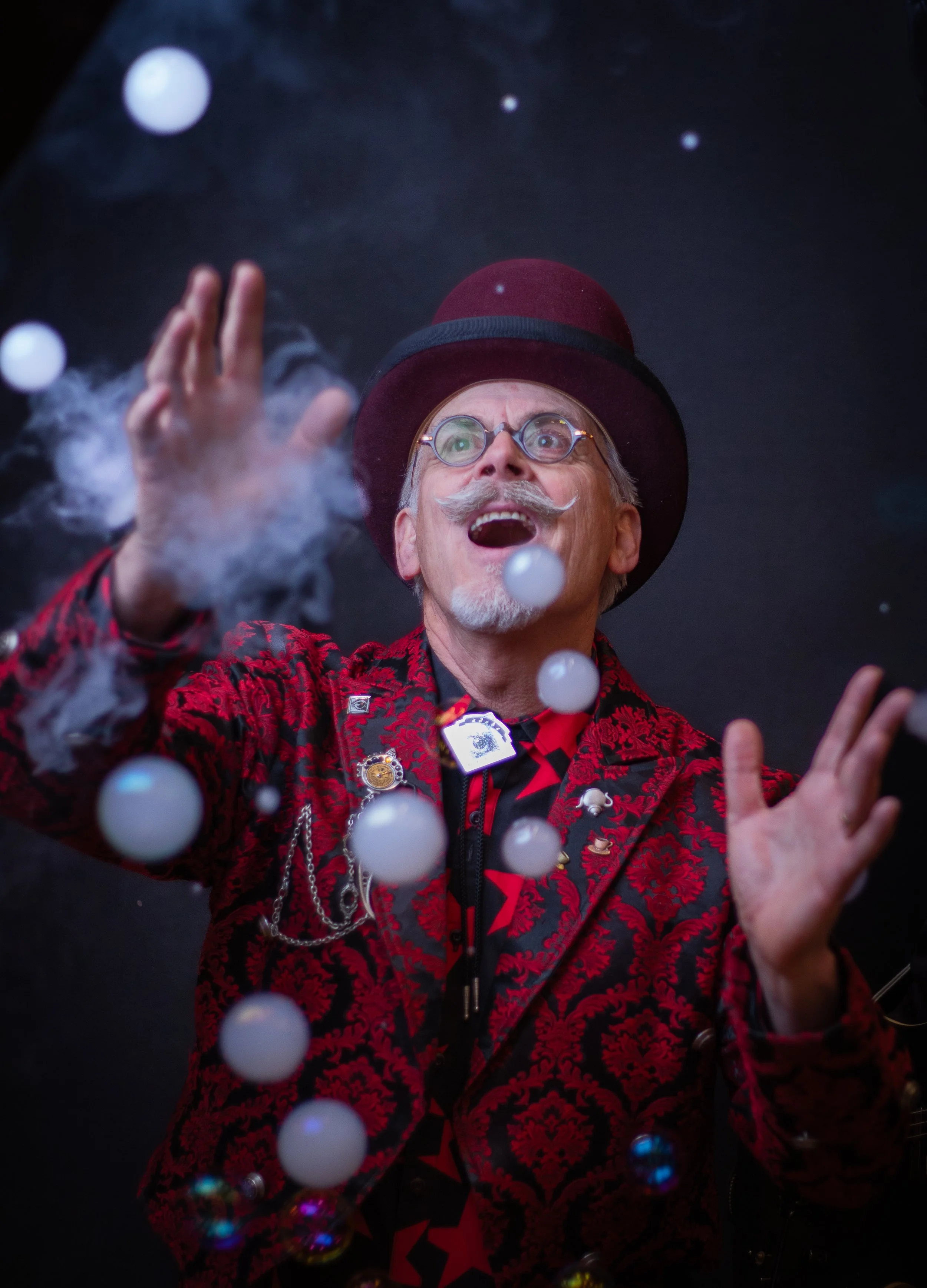 Steampunk man dressed wearing red jacket and looking at smoke and bubbles. WEaring glasses and a hat. Photo by high desert fantasy family photographer.