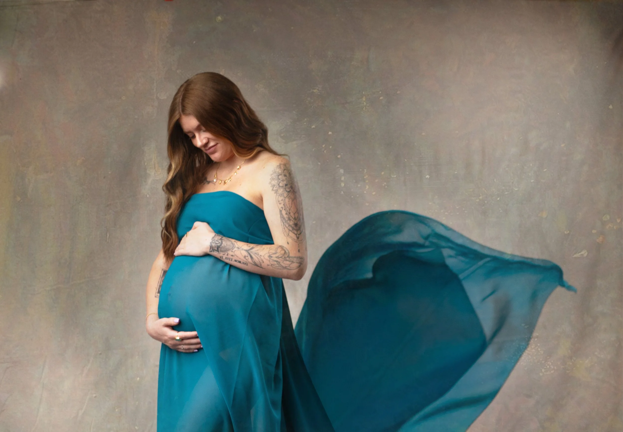 Maternity photo with fantasy fabric flowing while mama holds her belly, smiling. Photographer in the high desert, southern california.