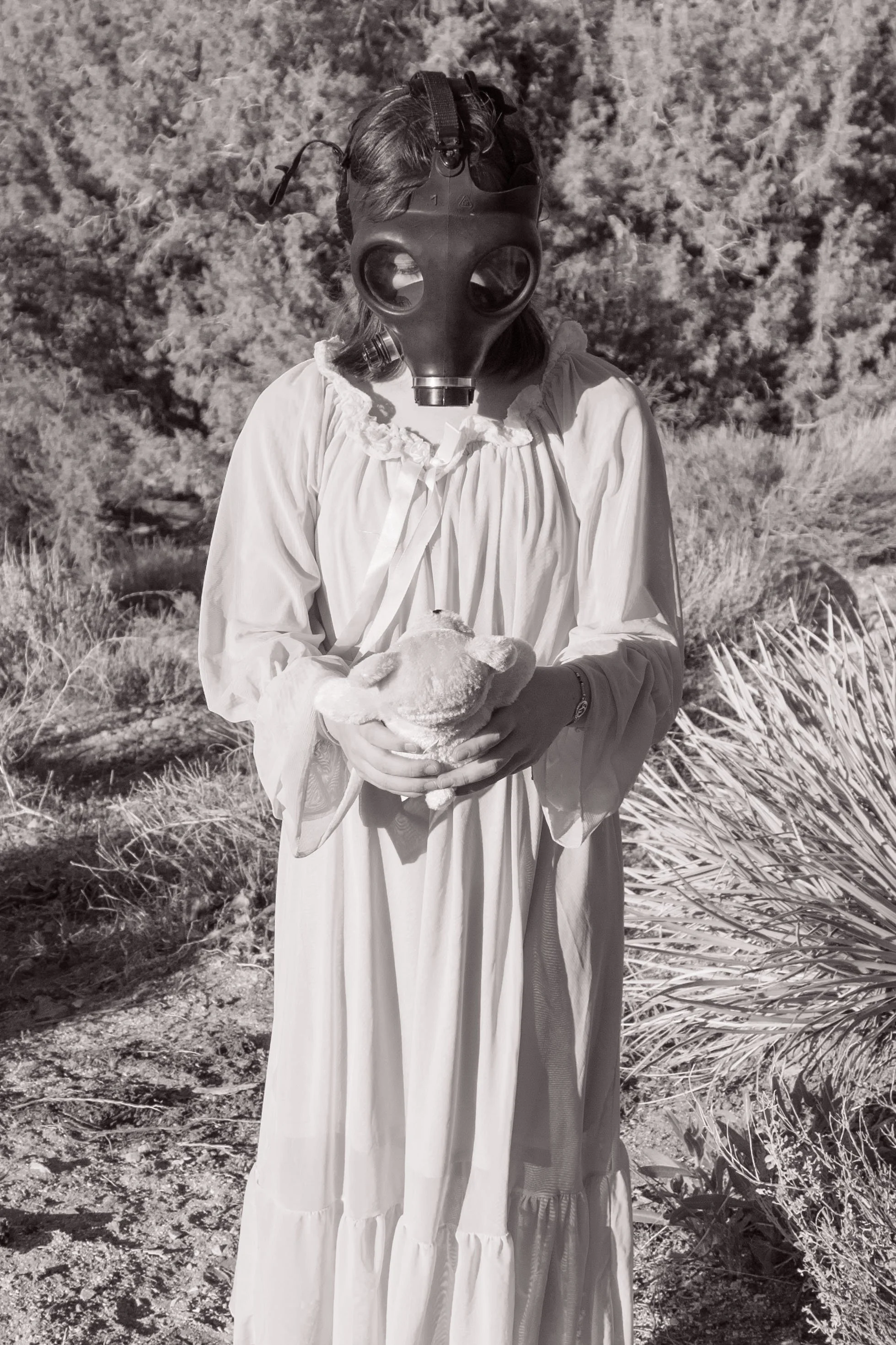 child holdig teddybeat while wearing gas mask