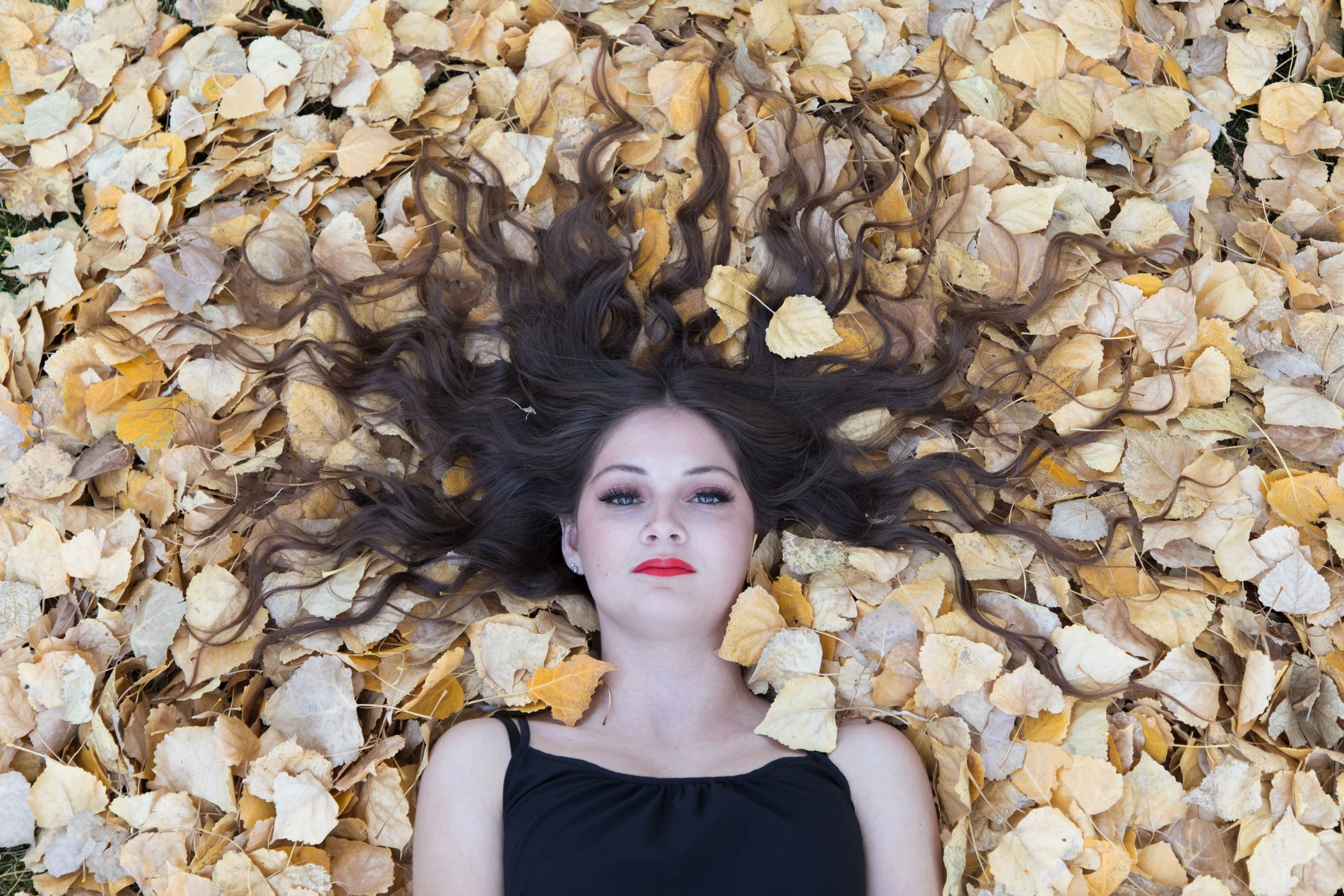 Woman laying in a pile of leaves with hair splayed looking like medusa.  Wrightwood photographer for fantasy lovers.