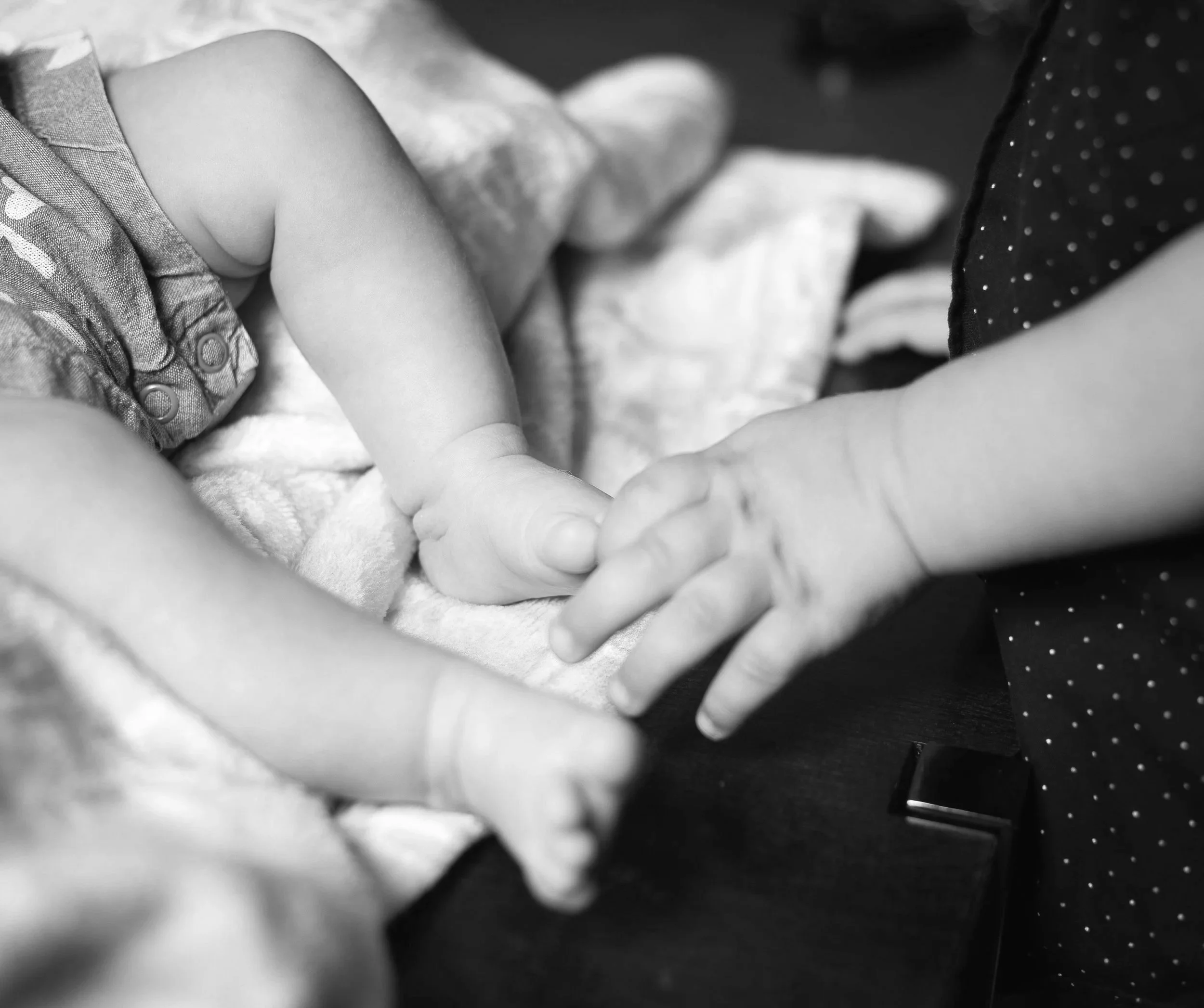 Toddler hand touching newborn toes, family in-home session. High desert family photographer takes playful photos.