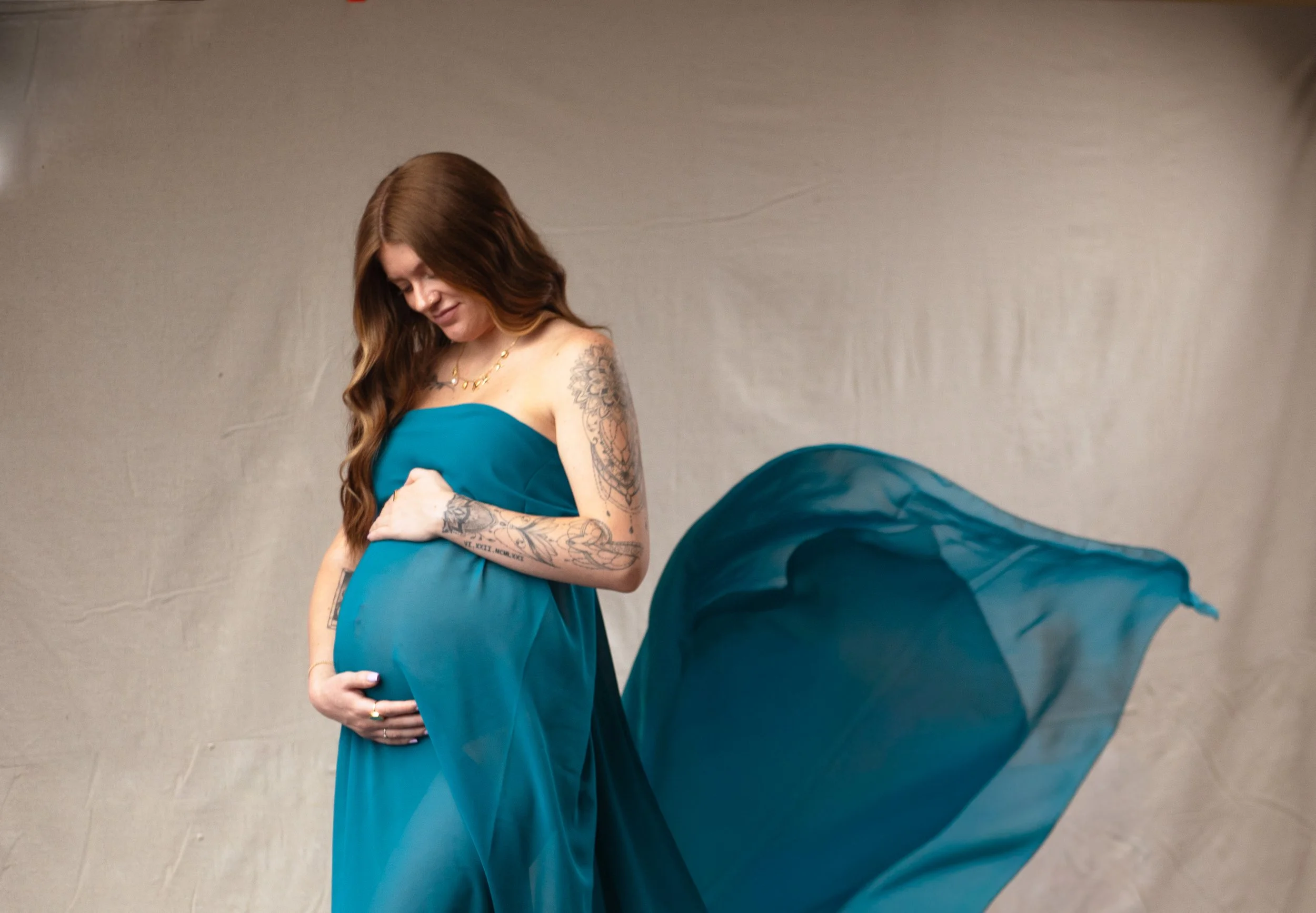 pregnant mother looking and holding belly in flowy blue gown