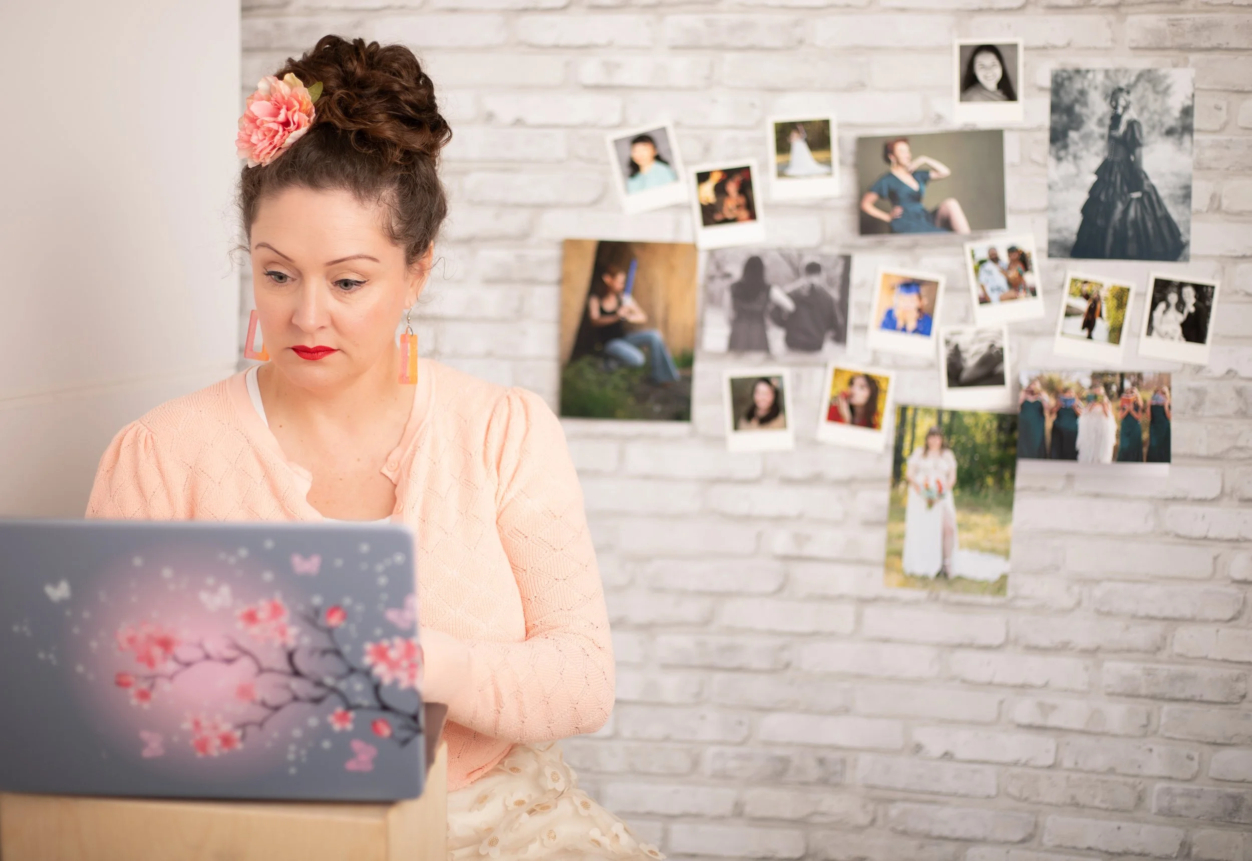 Fantasy photographer sitting at laptop editing images. Prints are displayed behind her on brick wall. Southern california photographer.
