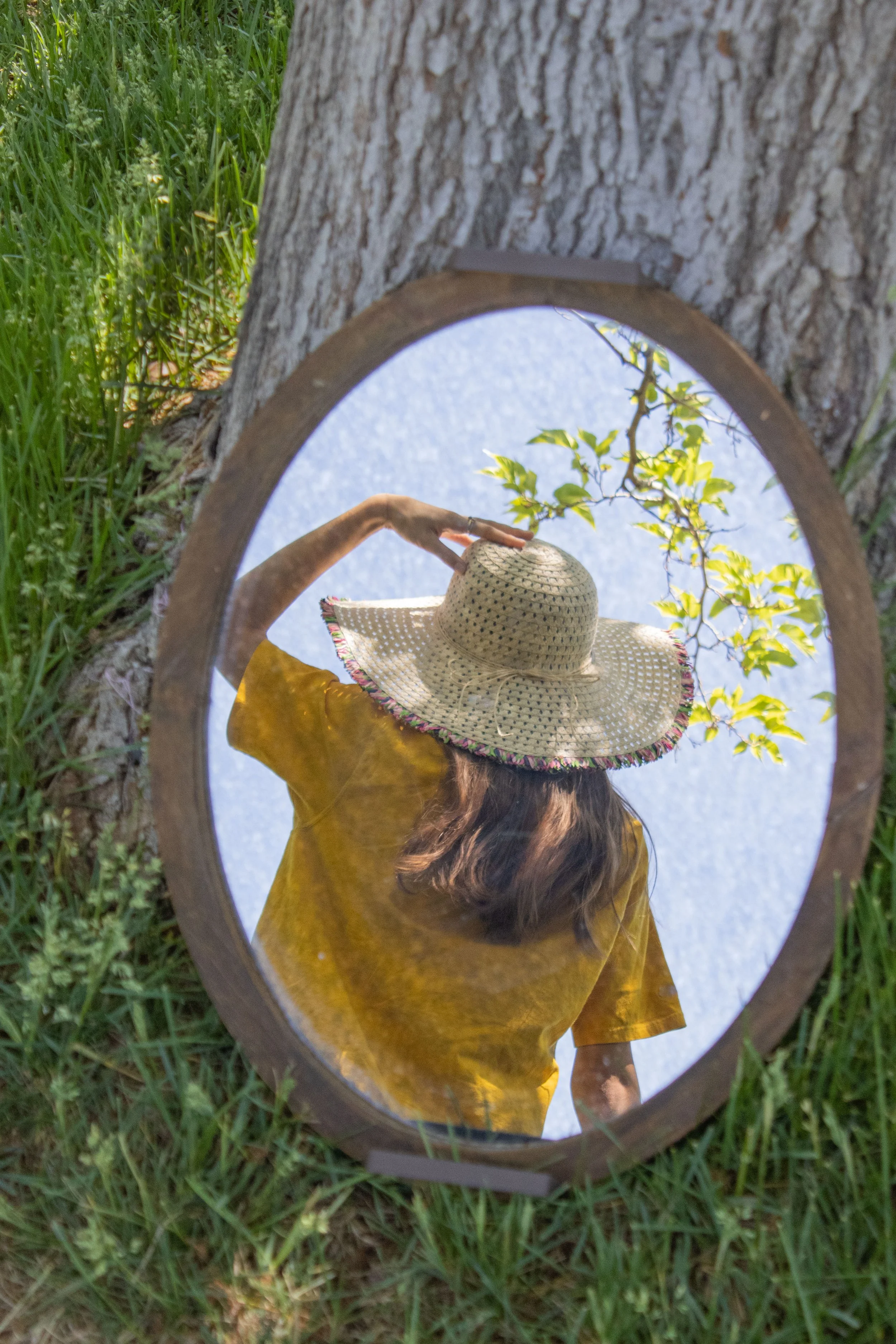 Storybook style photography by Annette Marie in the high desert, southern california. Woman holding a hat in mirror reflection leaned against a tree.