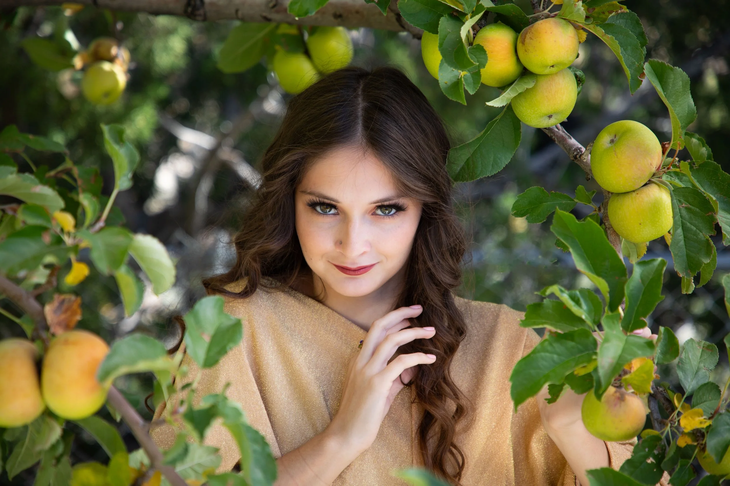 Woman wearing gold dress holding hair sitting the apple tree with evil look by annette marie fantasy photography.