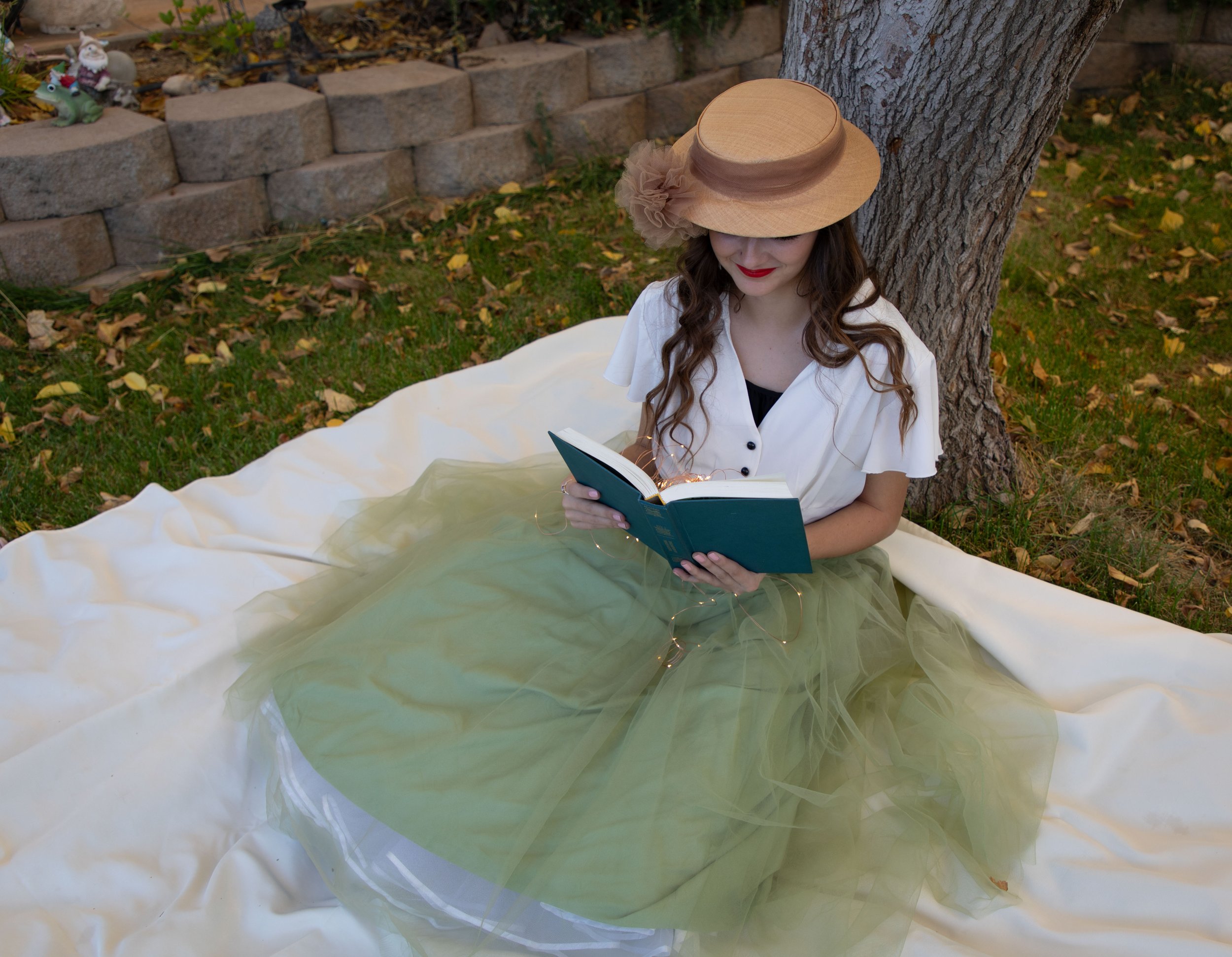 Woman reading a book wearing vintage clothing, and hat sitting on a blanket under a tree. Fantasy photography by Annette marie in the high desert, inland empire, southern california.