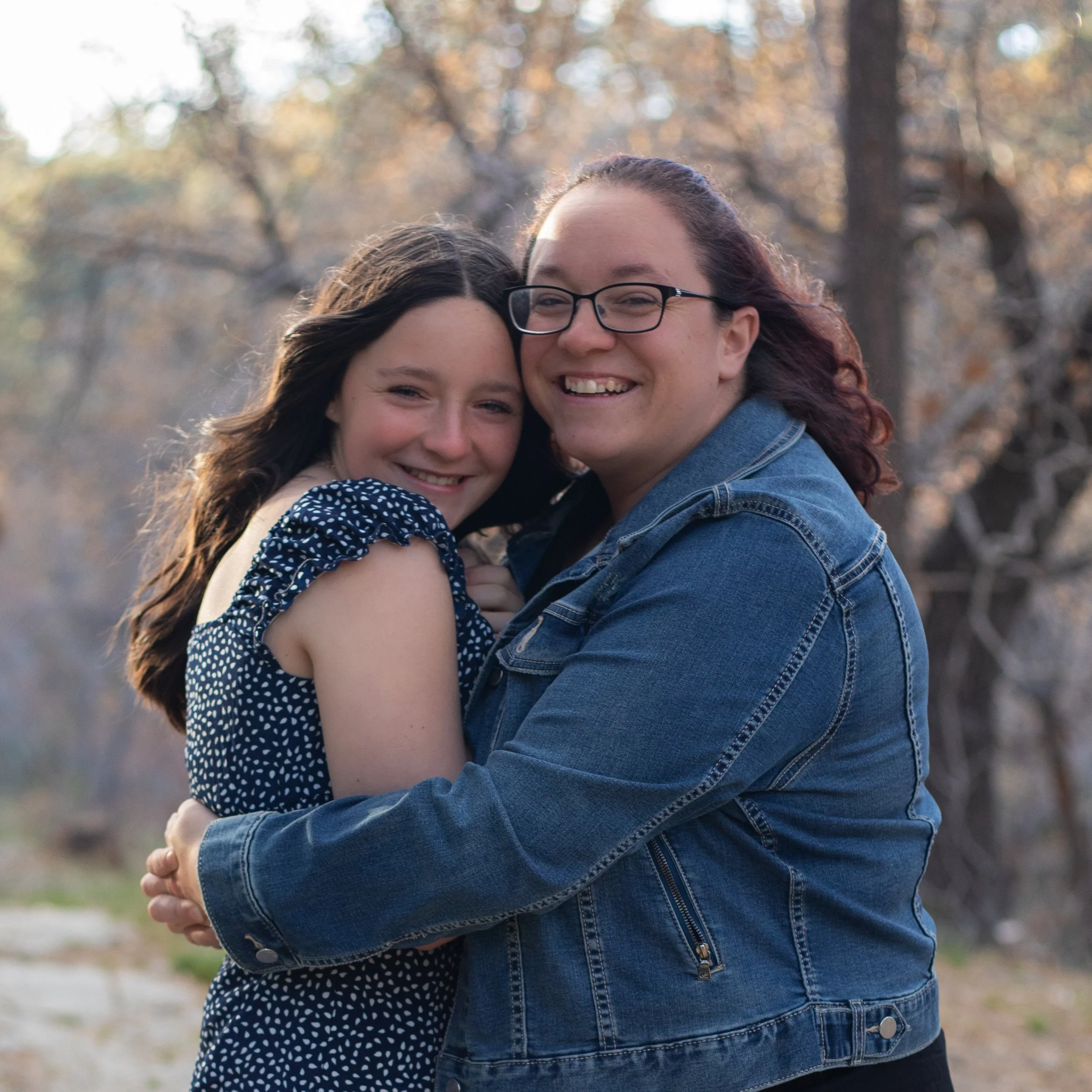 Mom hugging daughter tightly and smiling. Wearing blue denim outdoors in the high desert by family photographer.