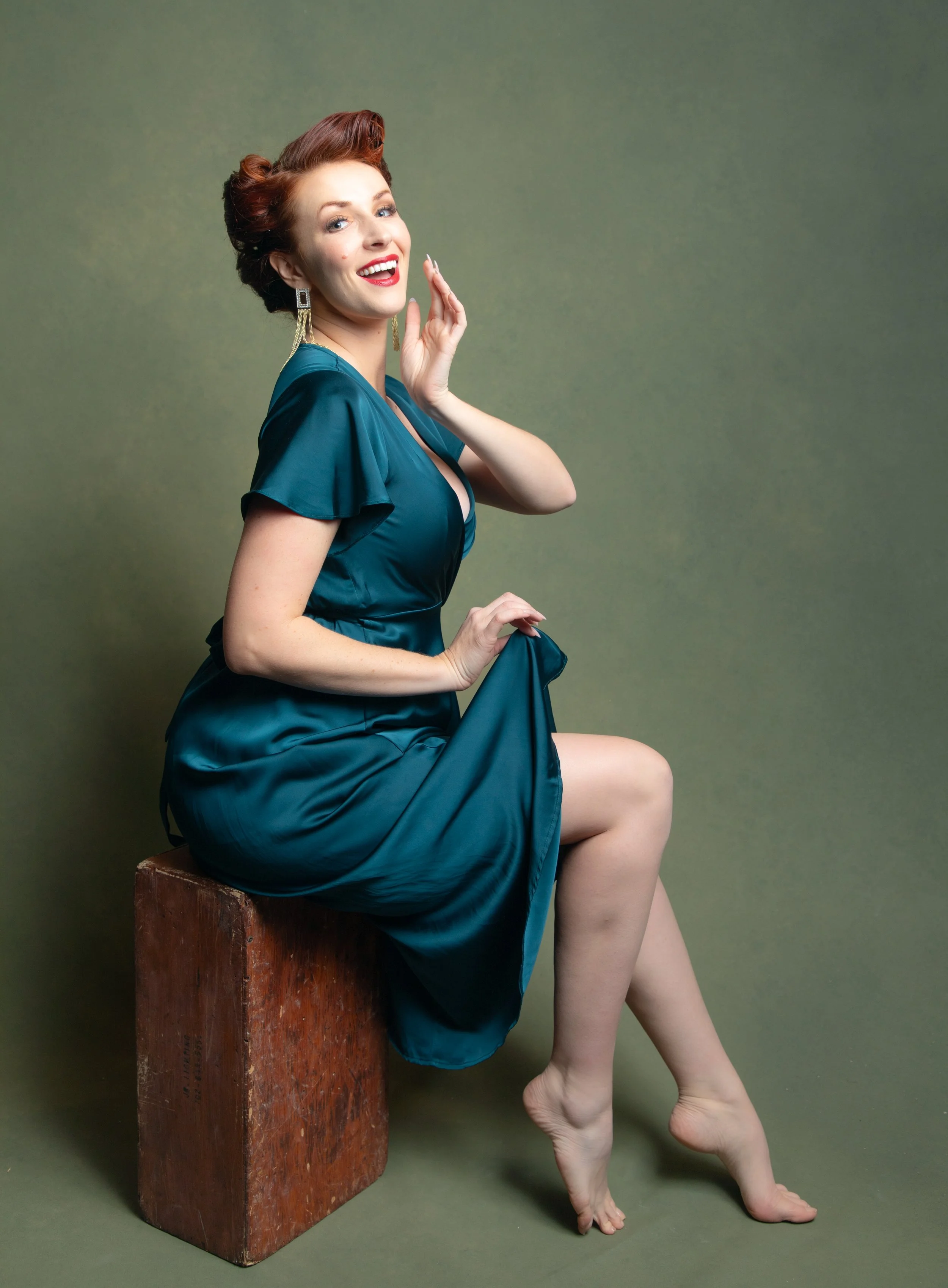 Woman dressed in pinup style with red hair and green dress sitting by fantasy photographer in inland empire, ca.